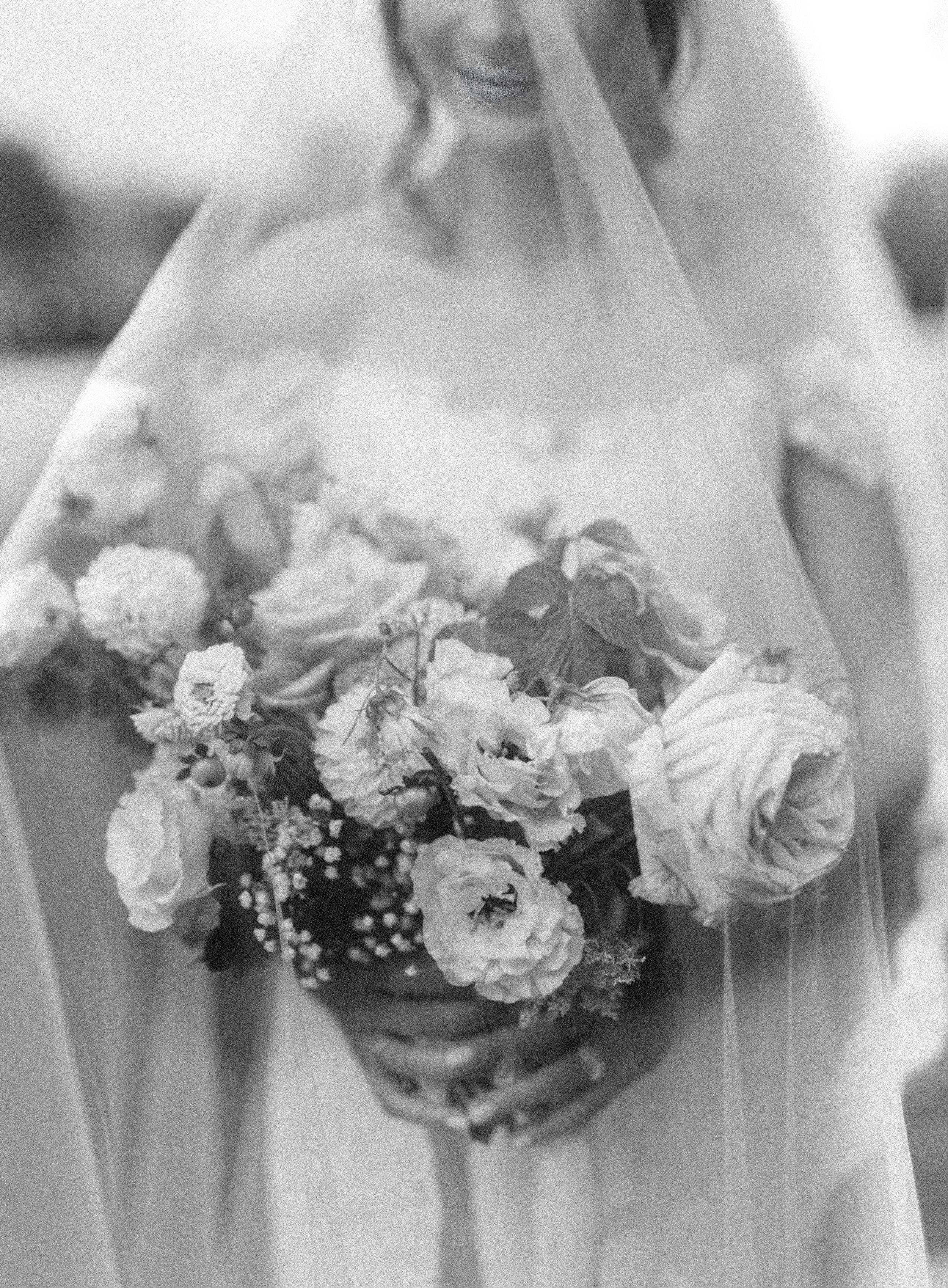 A bride holding a bouquet of flowers, mostly roses, behind her veil.