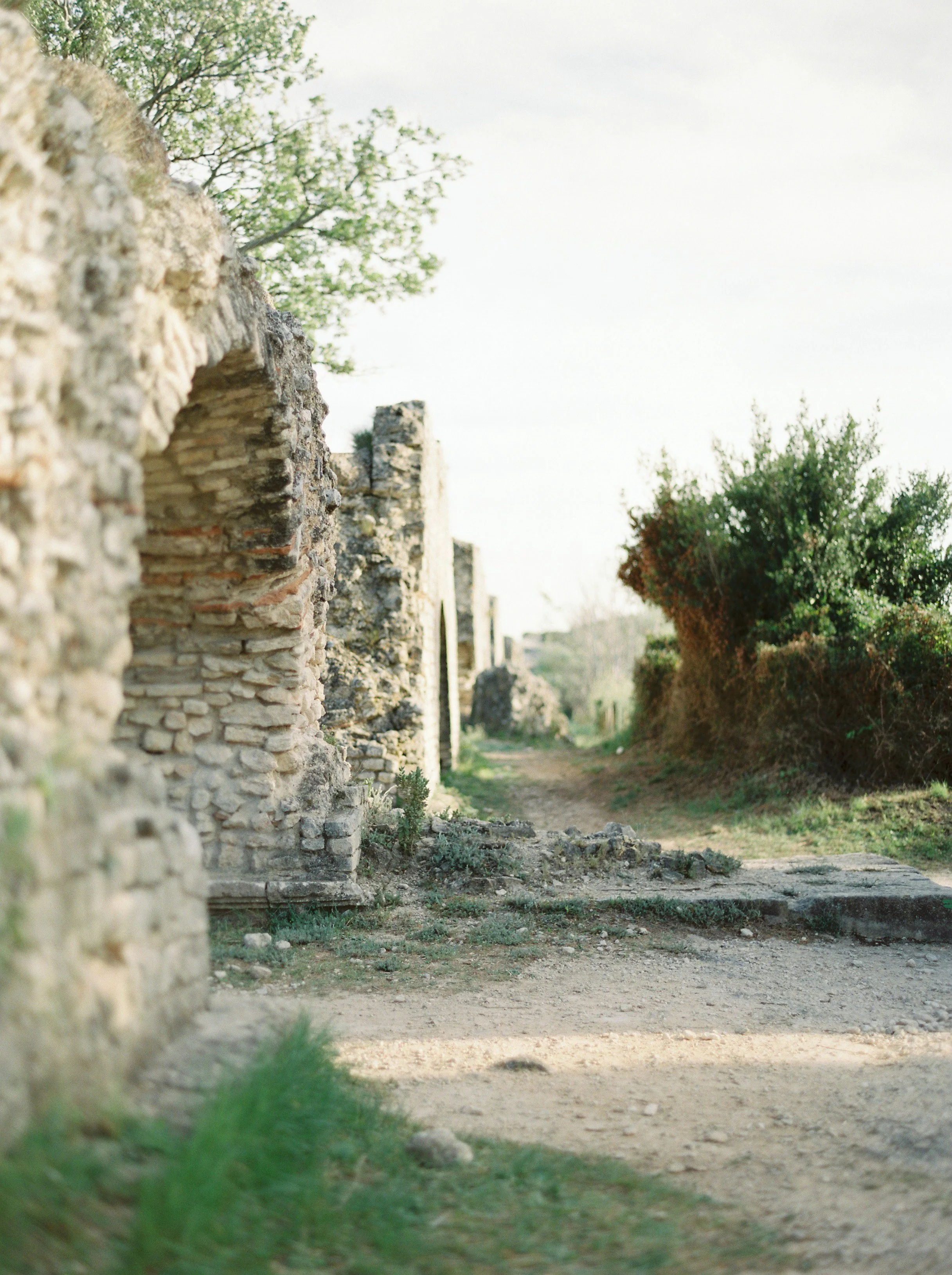 Ruins of an ancient stone structure with a dirt path and greenery.
