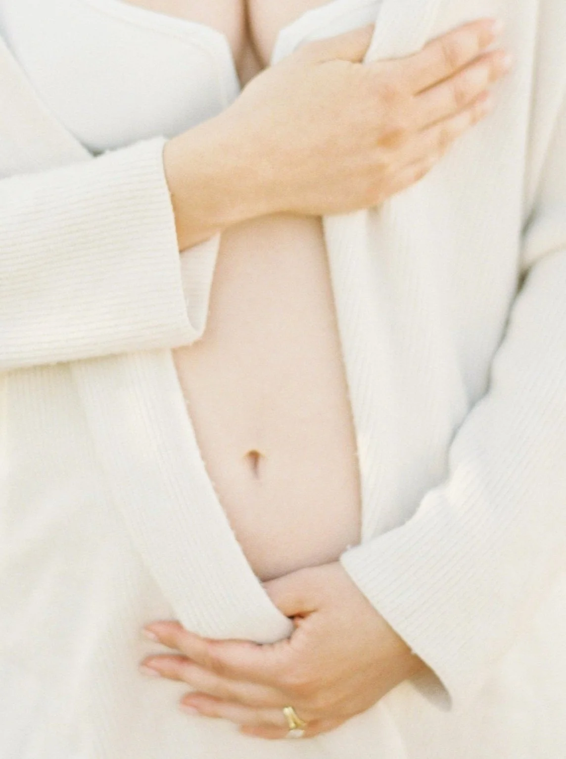 Close-up of a woman holding her hand on her heart and stomach area, wearing a white long-sleeve top.