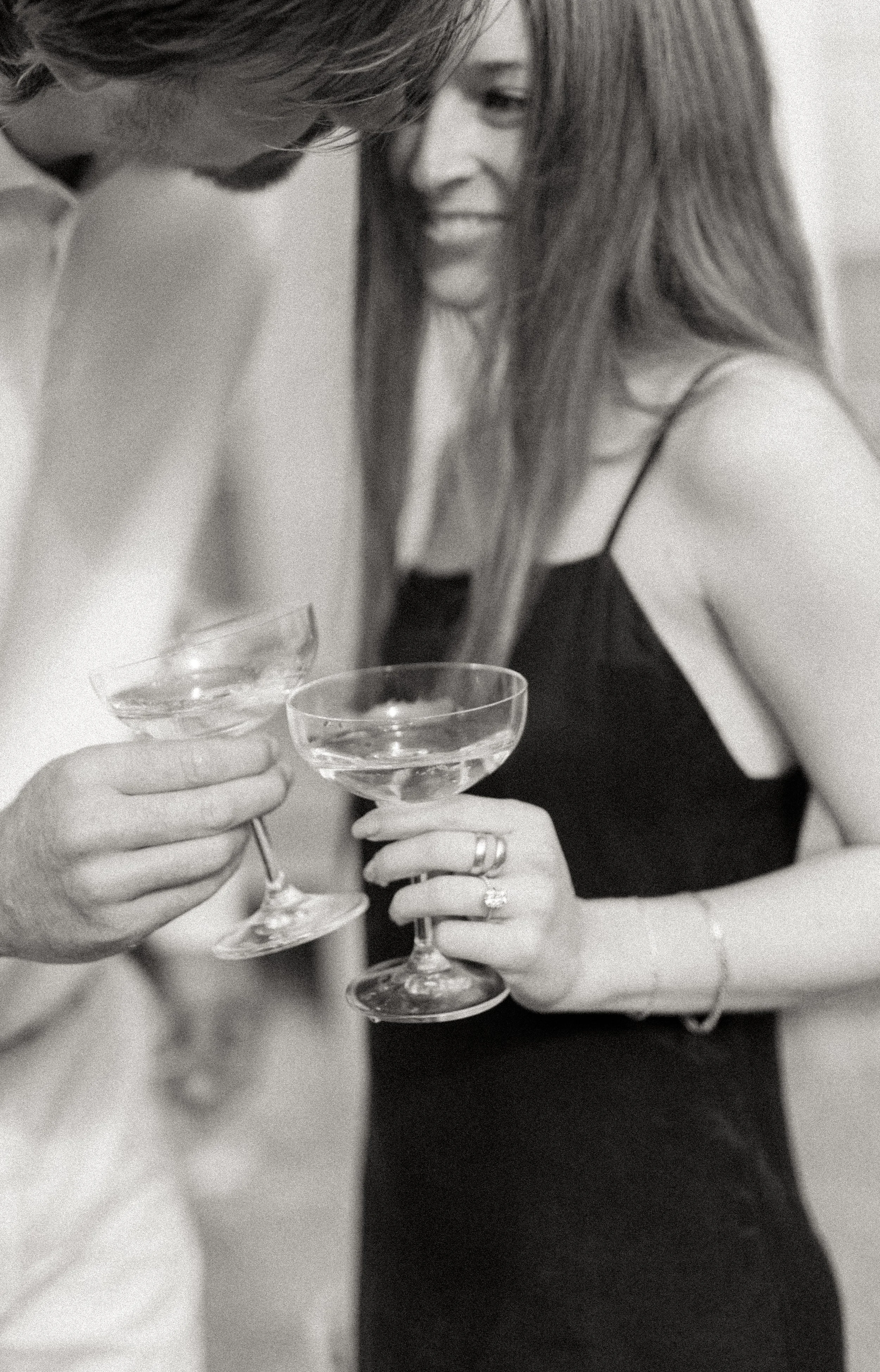 A black and white photo of a man and a woman holding champagne glasses, close together, at a celebration or party.