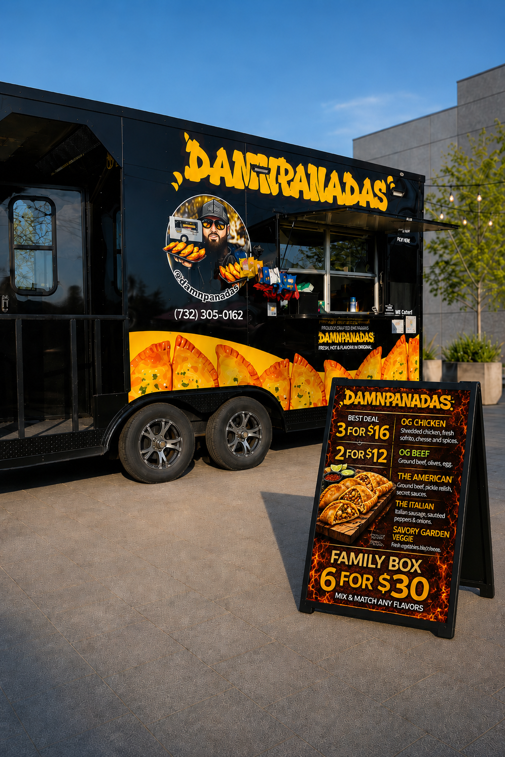 Black food truck named 'Damnpanadas' with colorful graphic of a man holding fresh empanadas, and menu board listing various options and prices outside on a sunny day.