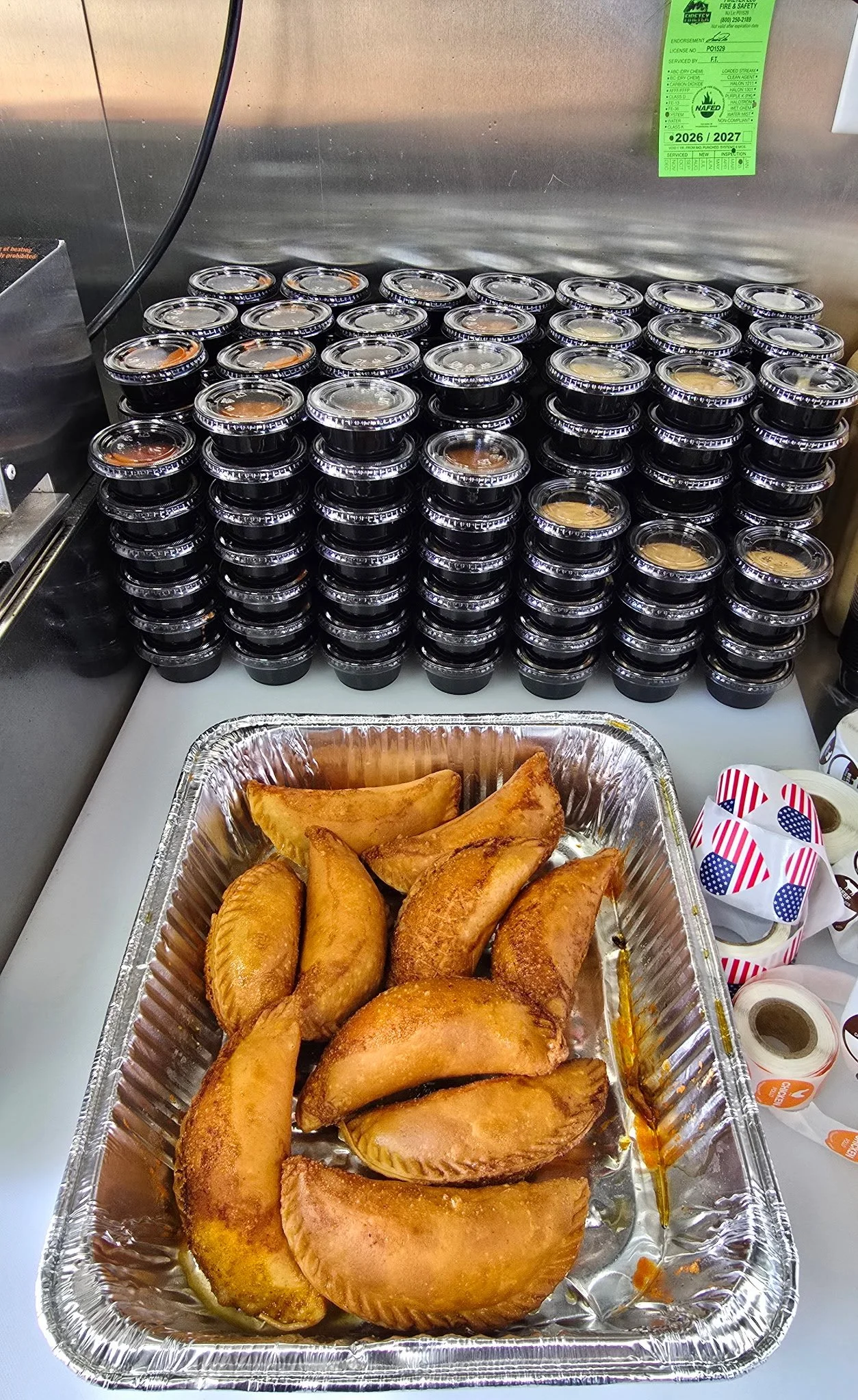 Tray of freshly fried golden empanadas with stacks of Damnpanadas dipping sauces in the background.