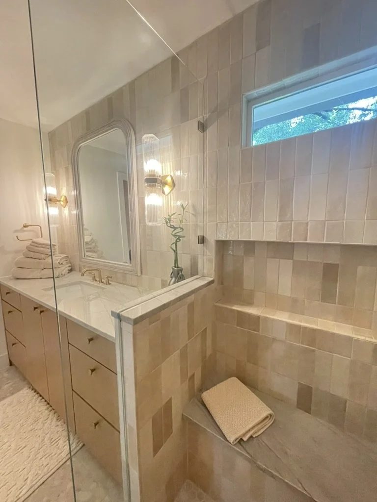Modern bathroom with beige tiles, mirror, vanity, and shower area.