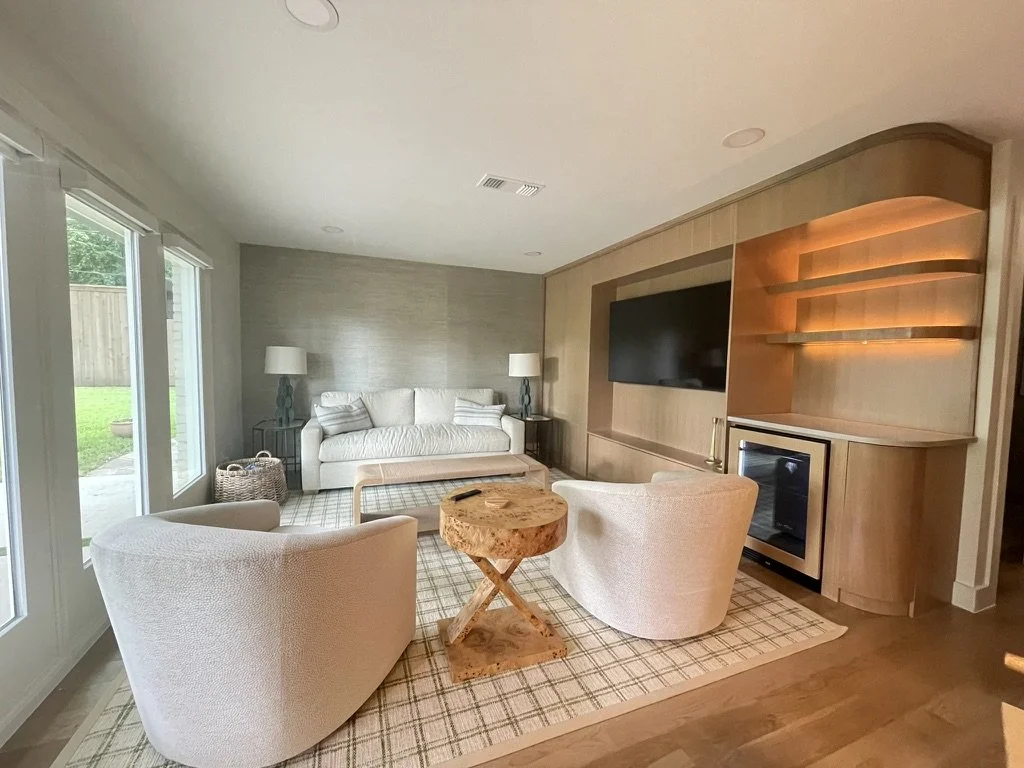 Modern living room with white armchairs, wooden coffee table, white sofa, wall-mounted TV, and built-in shelves.
