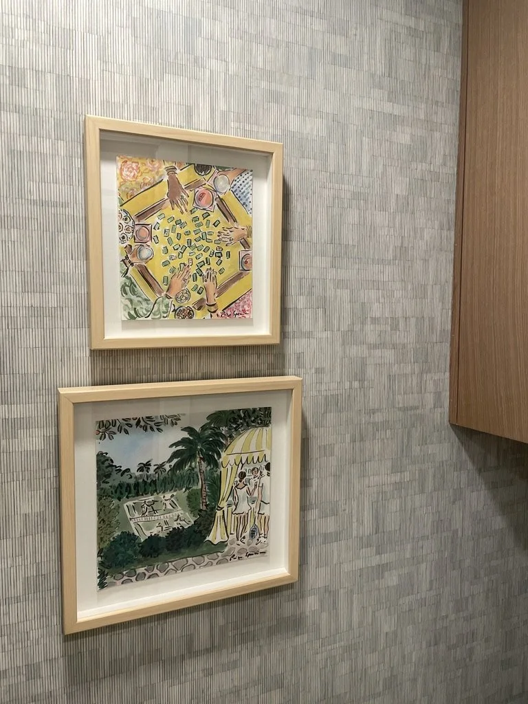 Two framed paintings on a textured wall; the top painting depicts a table with people playing a game, and the bottom painting shows an outdoor scene with people under a canopy near trees.