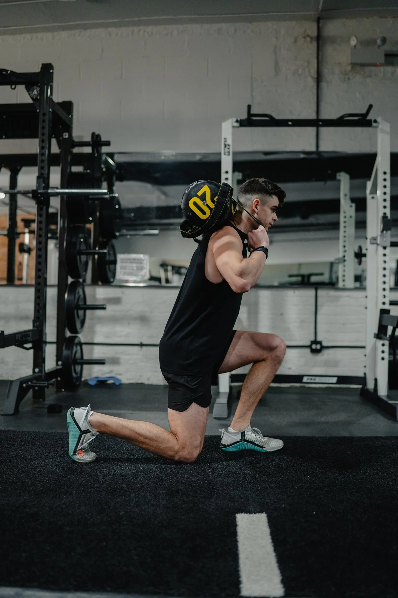 Man performing a lunge exercise with a weight on his back in a gym.