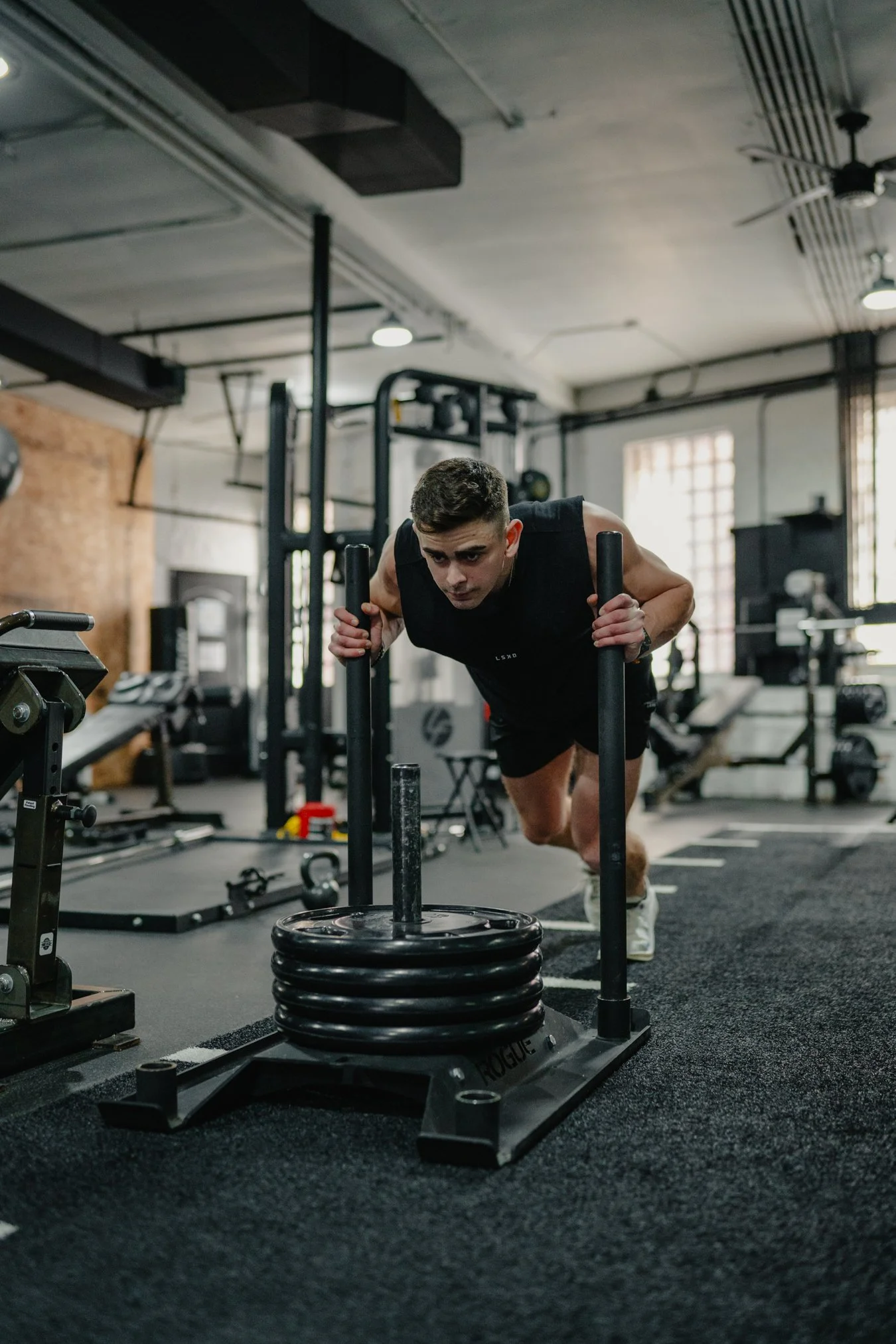 A man pushing a weighted sled in a gym, performing a workout.
