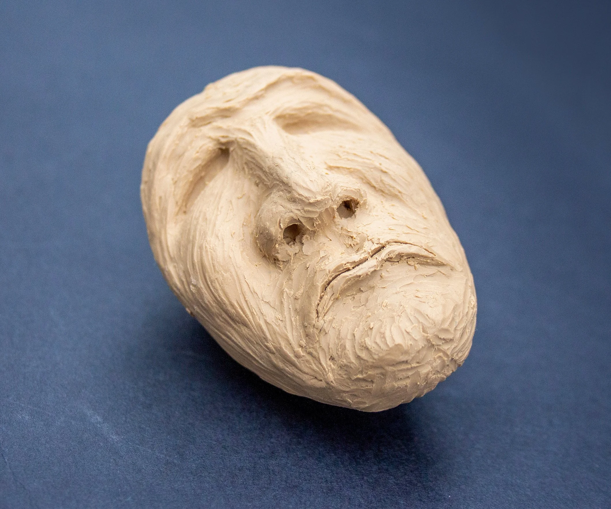 Clay sculpture of a human face with a beard on a blue background