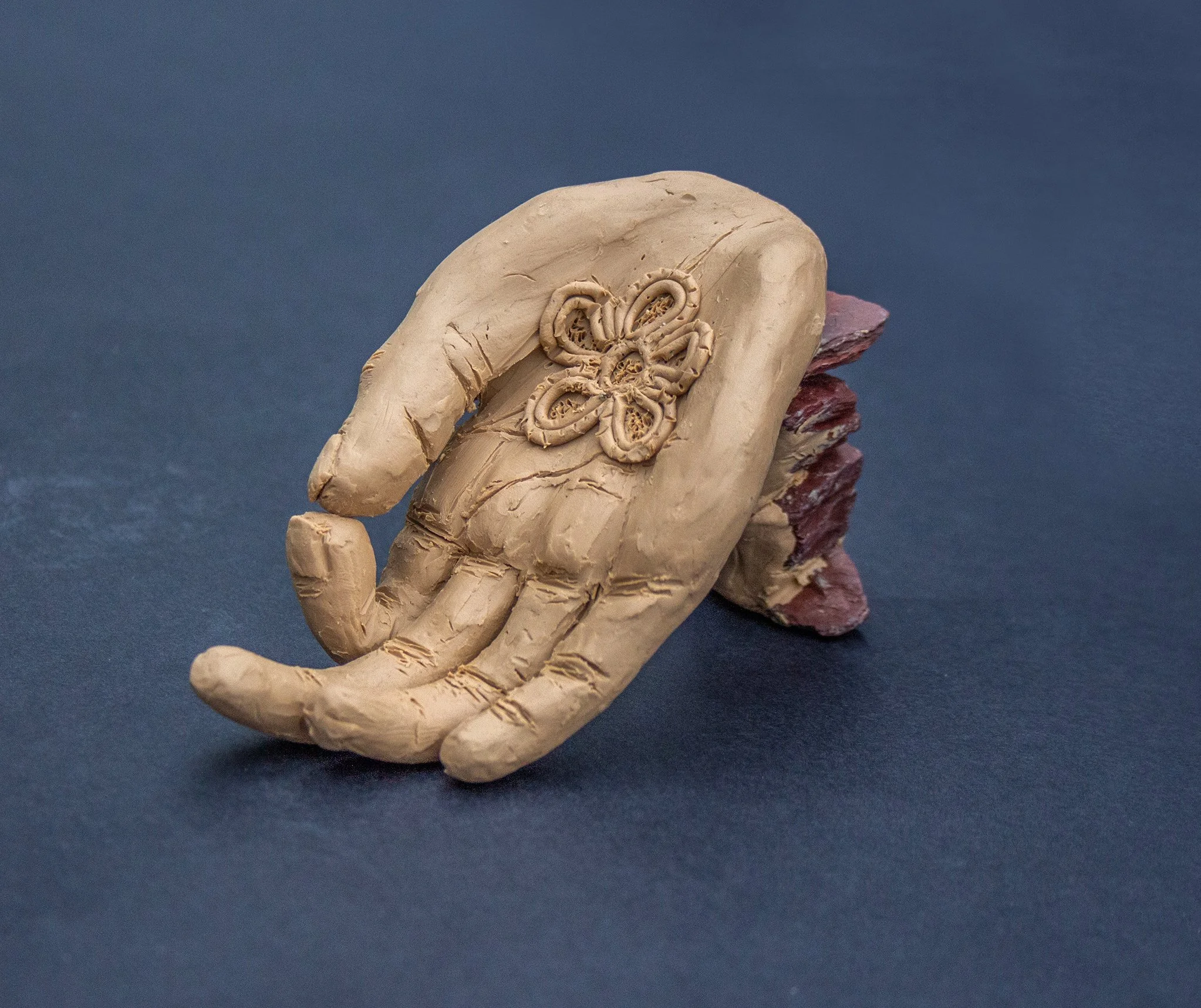 Sculpture of a hand with a flower carved on the palm, resting on a dark blue surface.