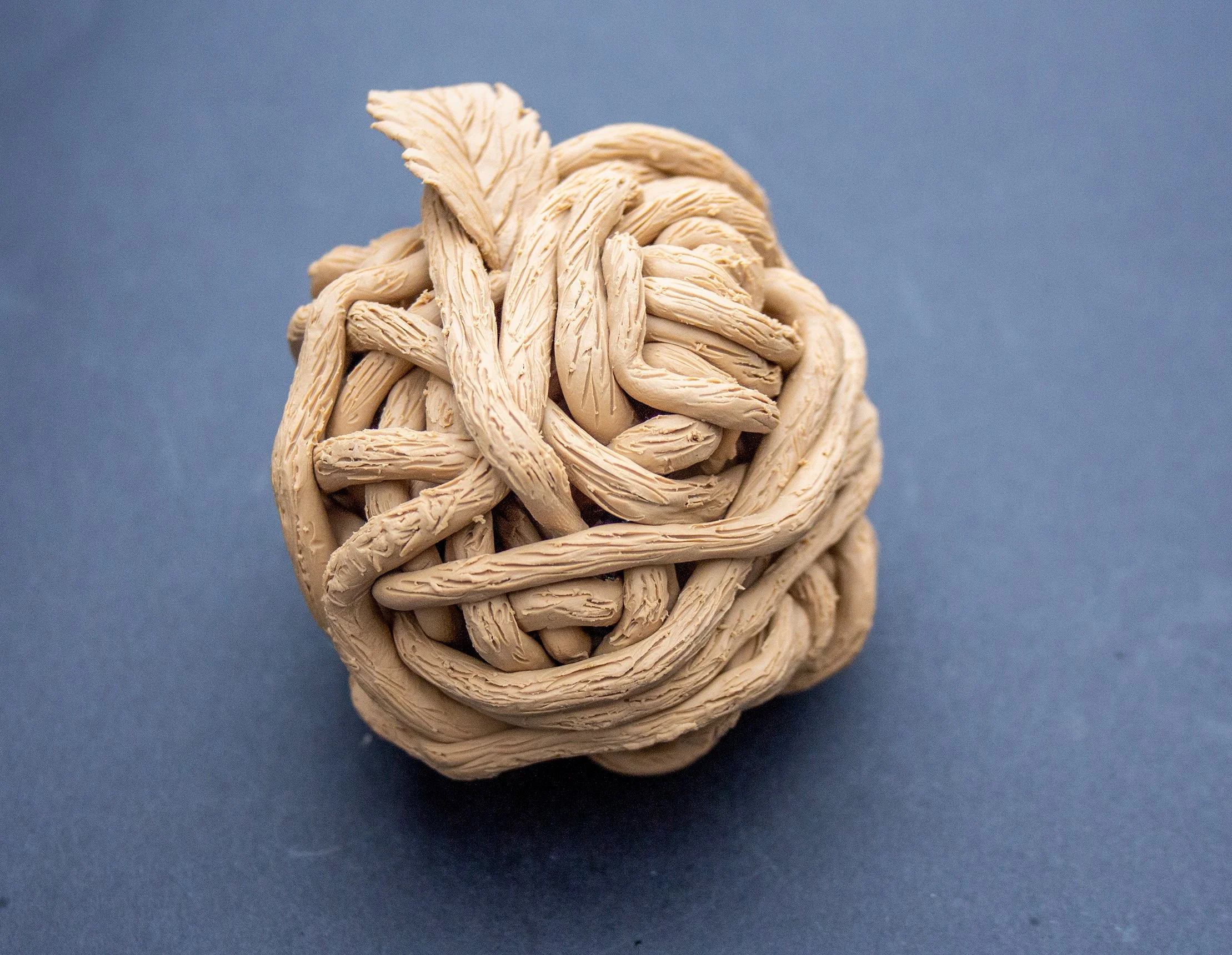 A tightly woven beige-colored ball made of textured, thick strands, placed on a blue background.