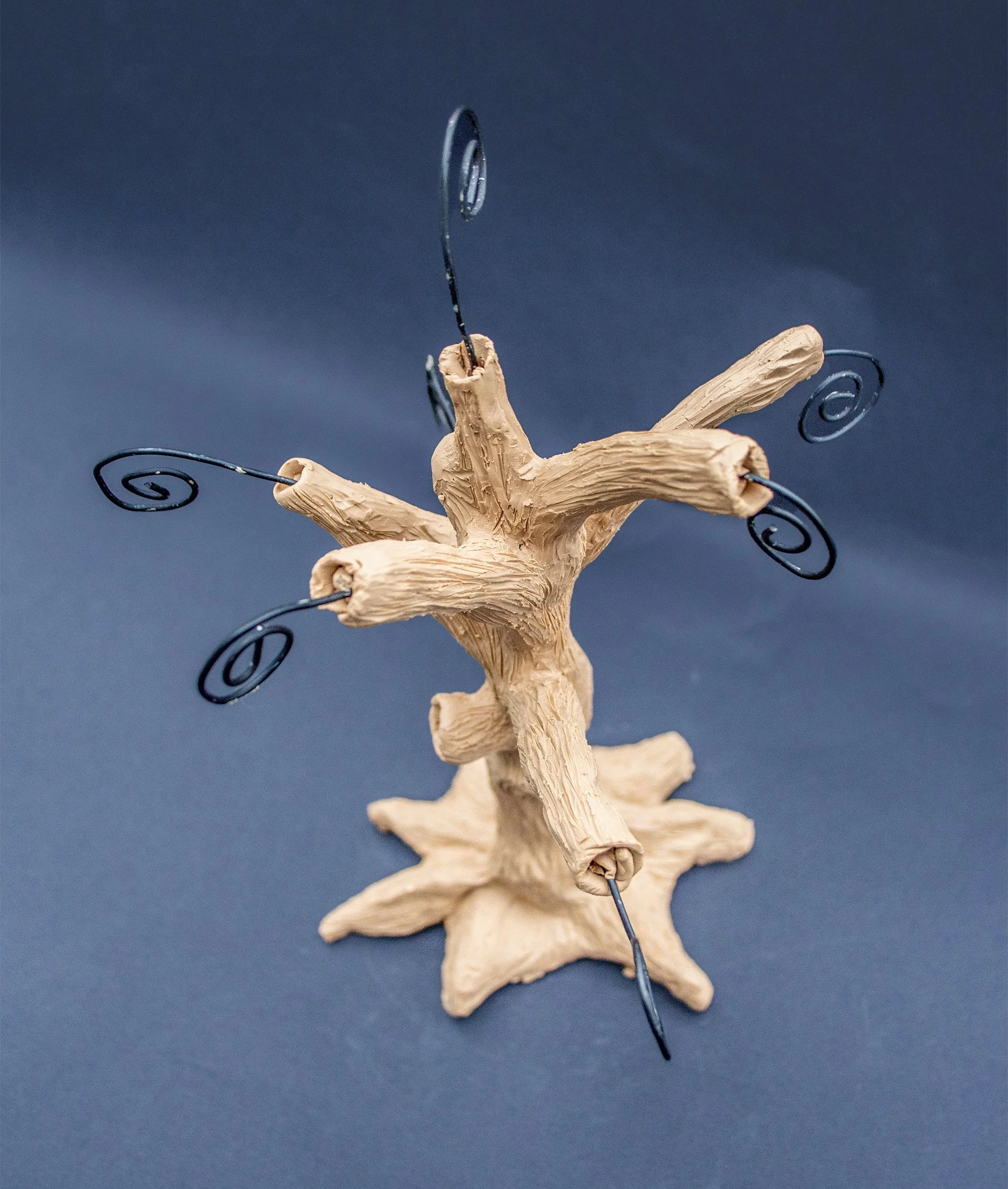 A decorative tree sculpture made of beige material with black wire swirls on the branches, standing on a star-shaped base.