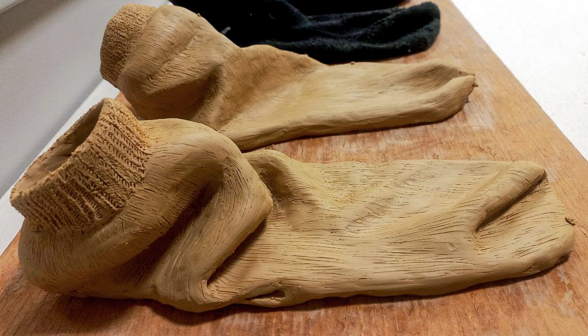 Wooden sculpture of an arm and hand with detailed finger and knuckle carvings on a wooden surface.