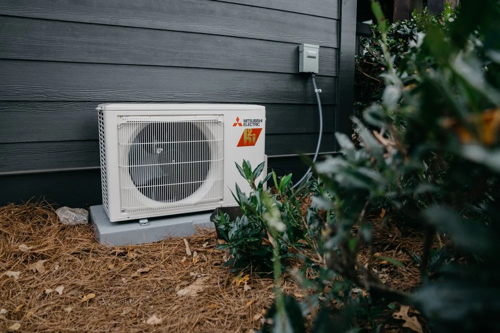 HVAC technician installing an outdoor cold-climate heat pump at a Southern Maine residence.