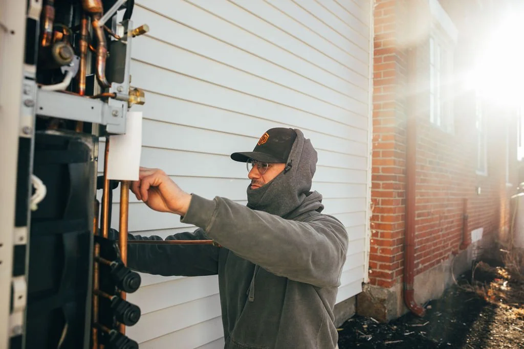 Heat pump technician servicing an outdoor unit before winter in Maine.