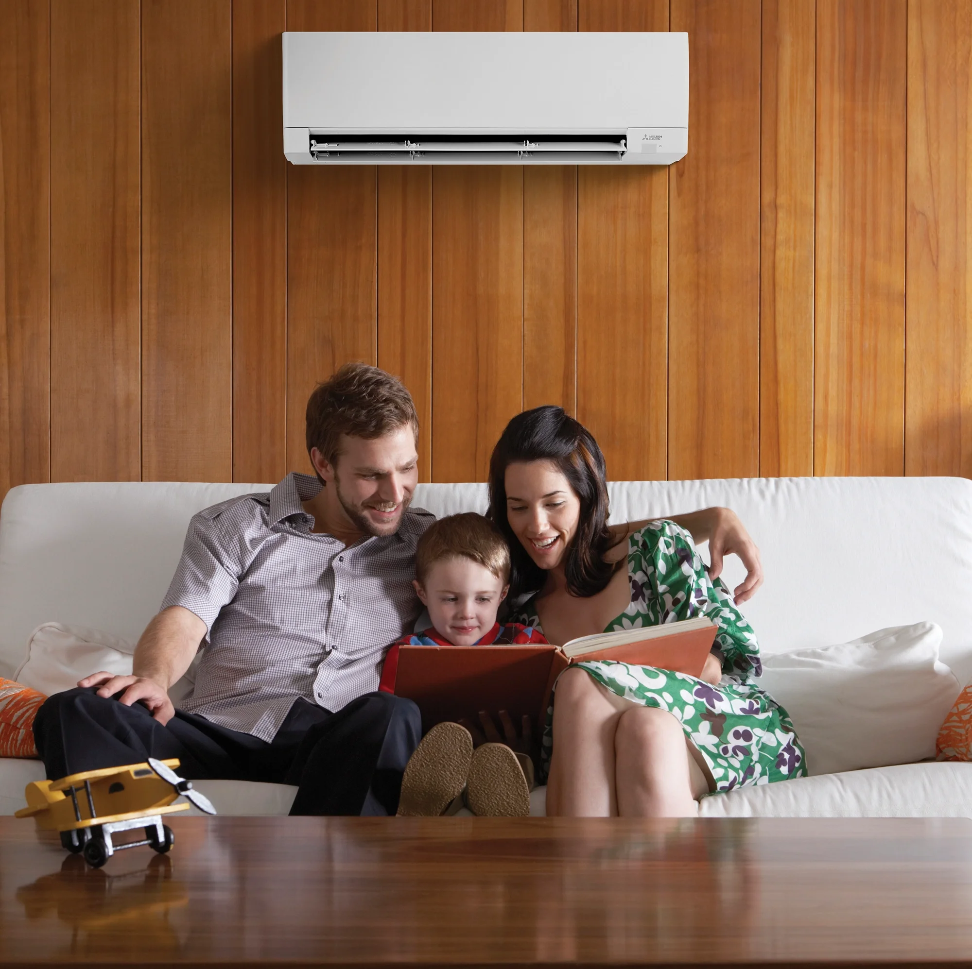 Family relaxing at home beneath a wall-mounted heat pump used for comfortable heating.