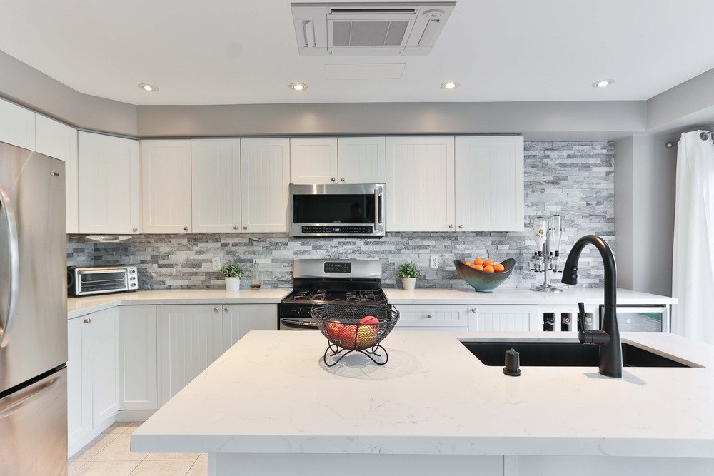 Ceiling-mounted cassette heat pump installed in a modern kitchen with white cabinets, providing ductless heating and cooling for a residential home.