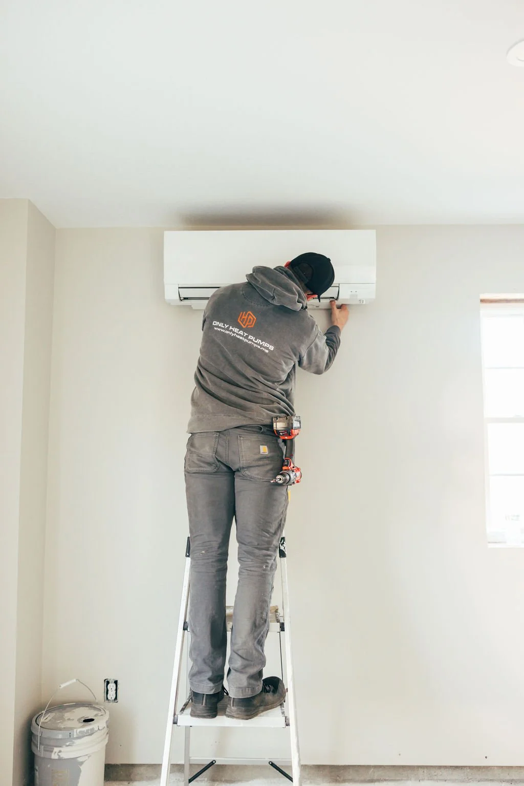 Only Heat Pumps technician servicing a wall-mounted ductless mini-split system in a Southern Maine home.