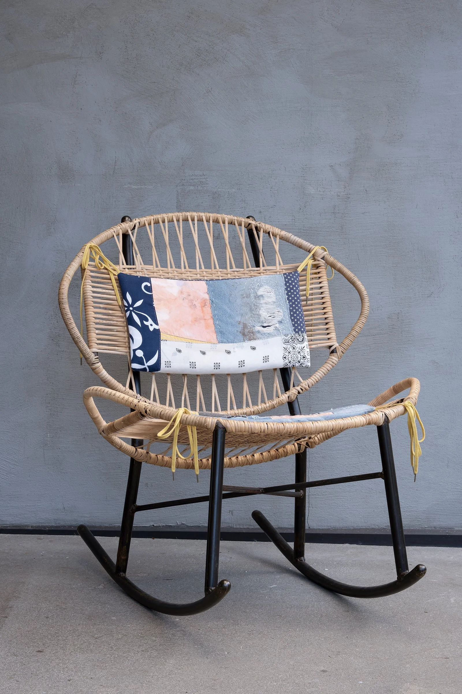 Clamshell rocking chair with cane-woven seat and back, featuring colorful Sashiko-style embroidered cushions for a bold, artisan-inspired look.