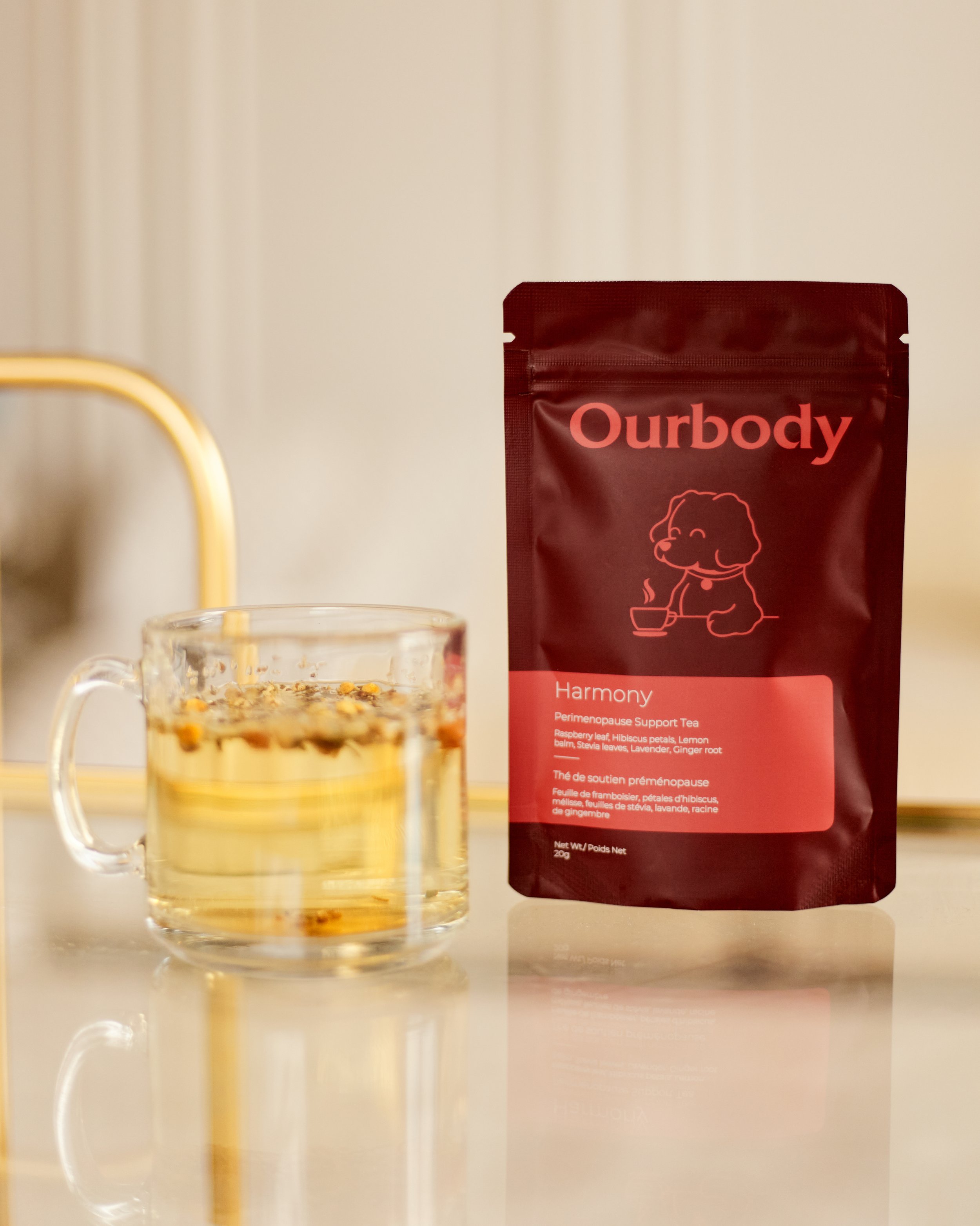A package of Ourbody Harmony Perimenopause Support Tea next to a glass mug filled with brewed tea on a white surface.