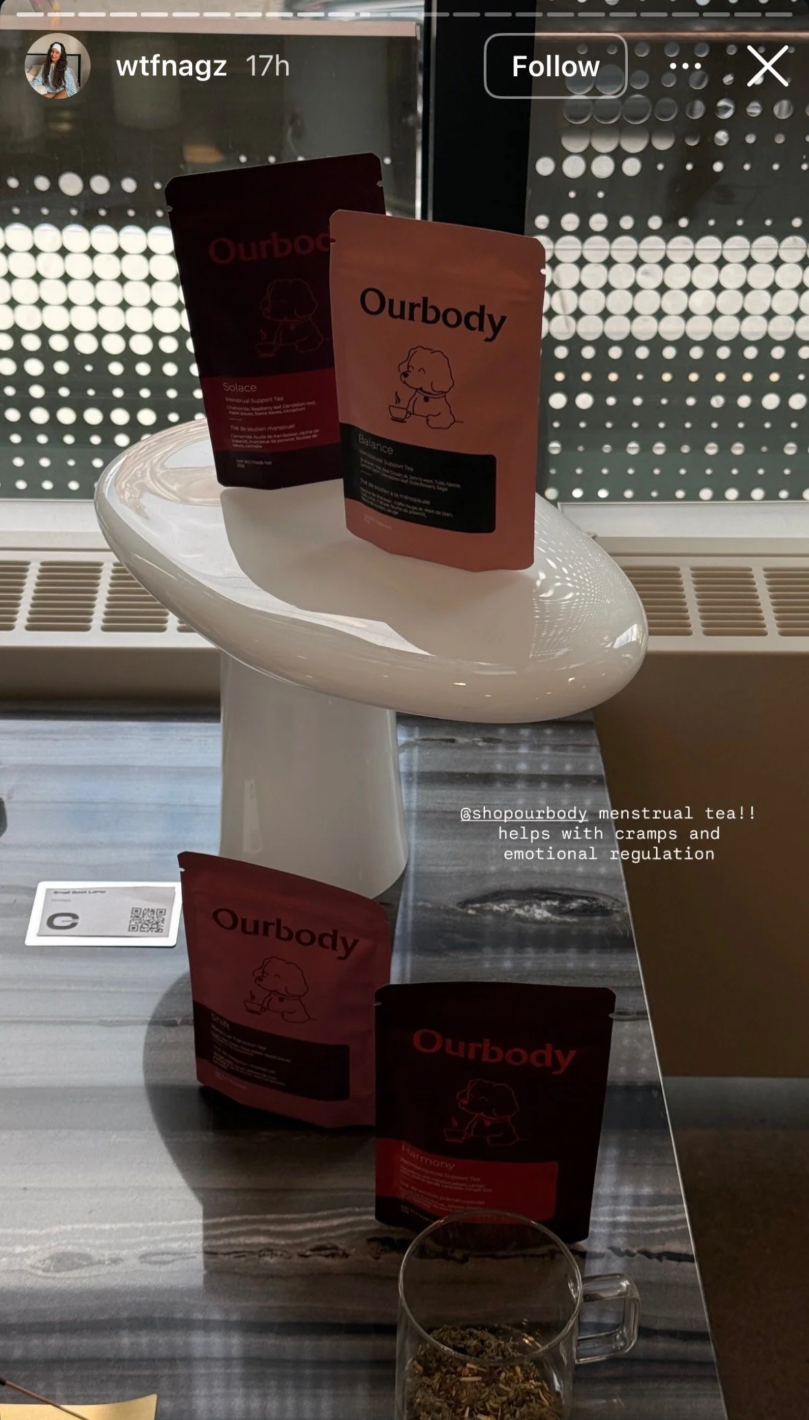 Display of Ourbody herbal tea packets on a white pedestal and a table, with a clear glass cup filled with herbal tea and text overlay promoting menstrual tea for cramps and emotional regulation.