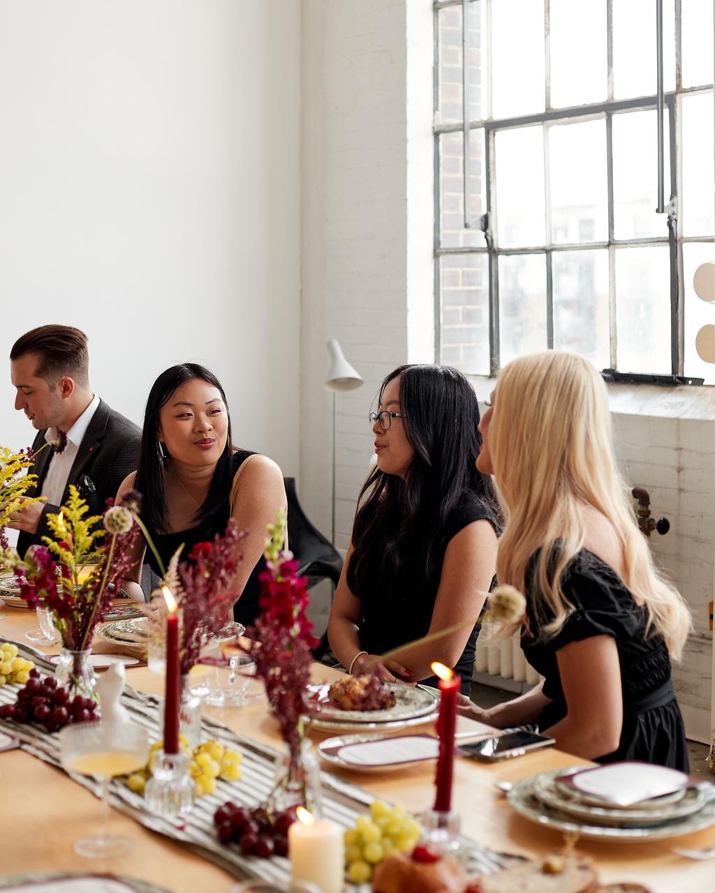People sitting at a decorated dining table with candles and flowers in a bright room.