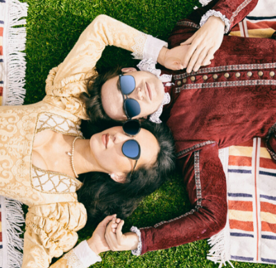 Promotonal image for Pop-up Globe's final season "The Summer of Love" depicting Romeo and Juliet lying on the grass in Jacobean costume, with modern sunglasses.