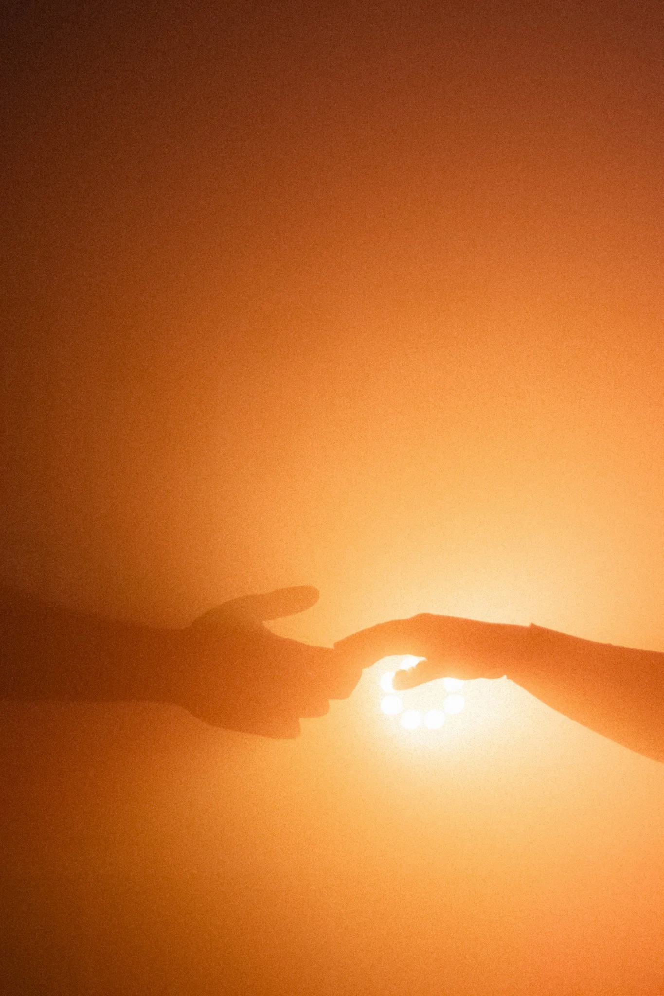Silhouettes of two hands reaching towards each other with a bright light in the background.