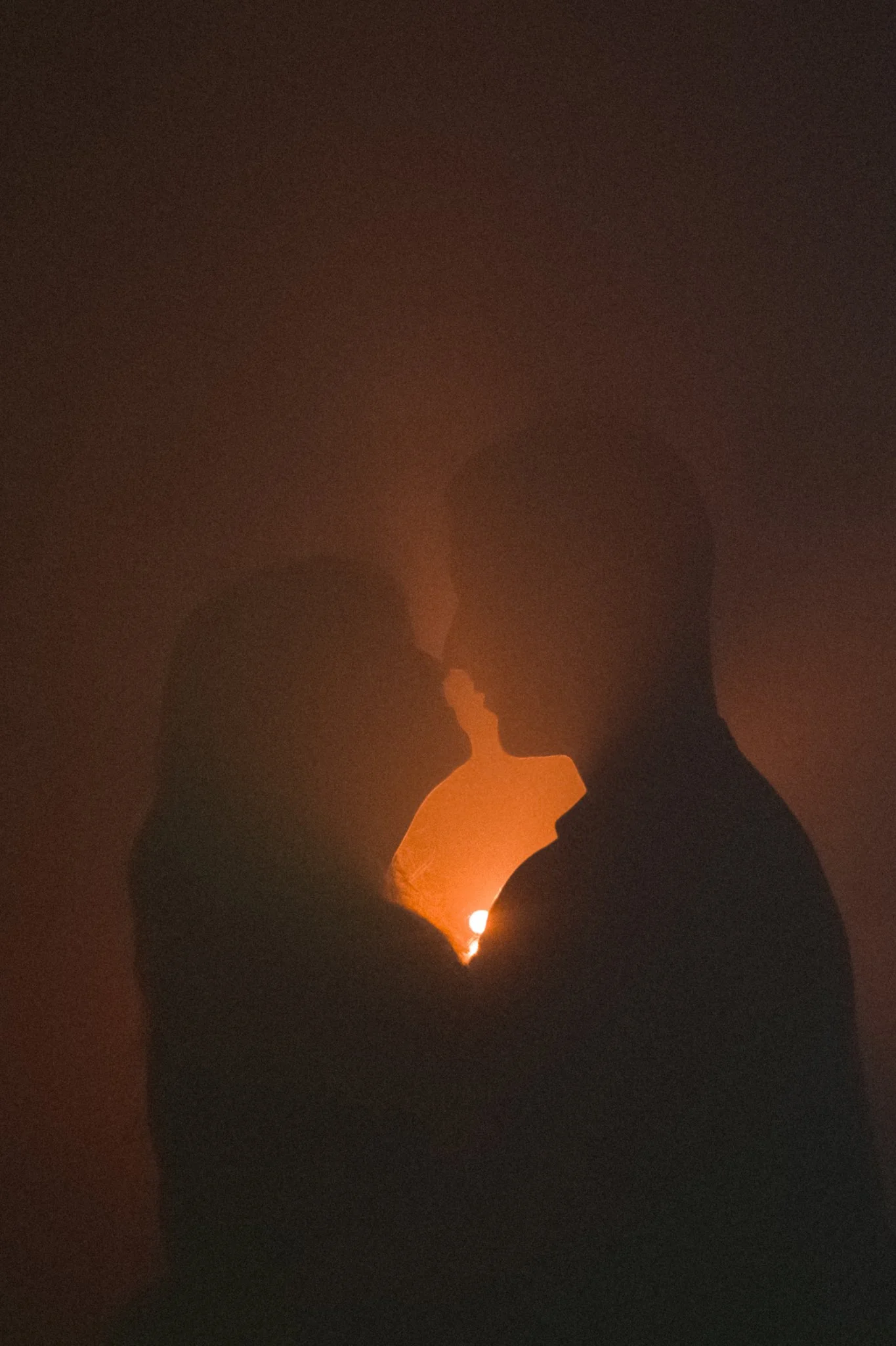 Silhouettes of three people with foreheads touching, backlit by warm orange light, creating a romantic or intimate scene.