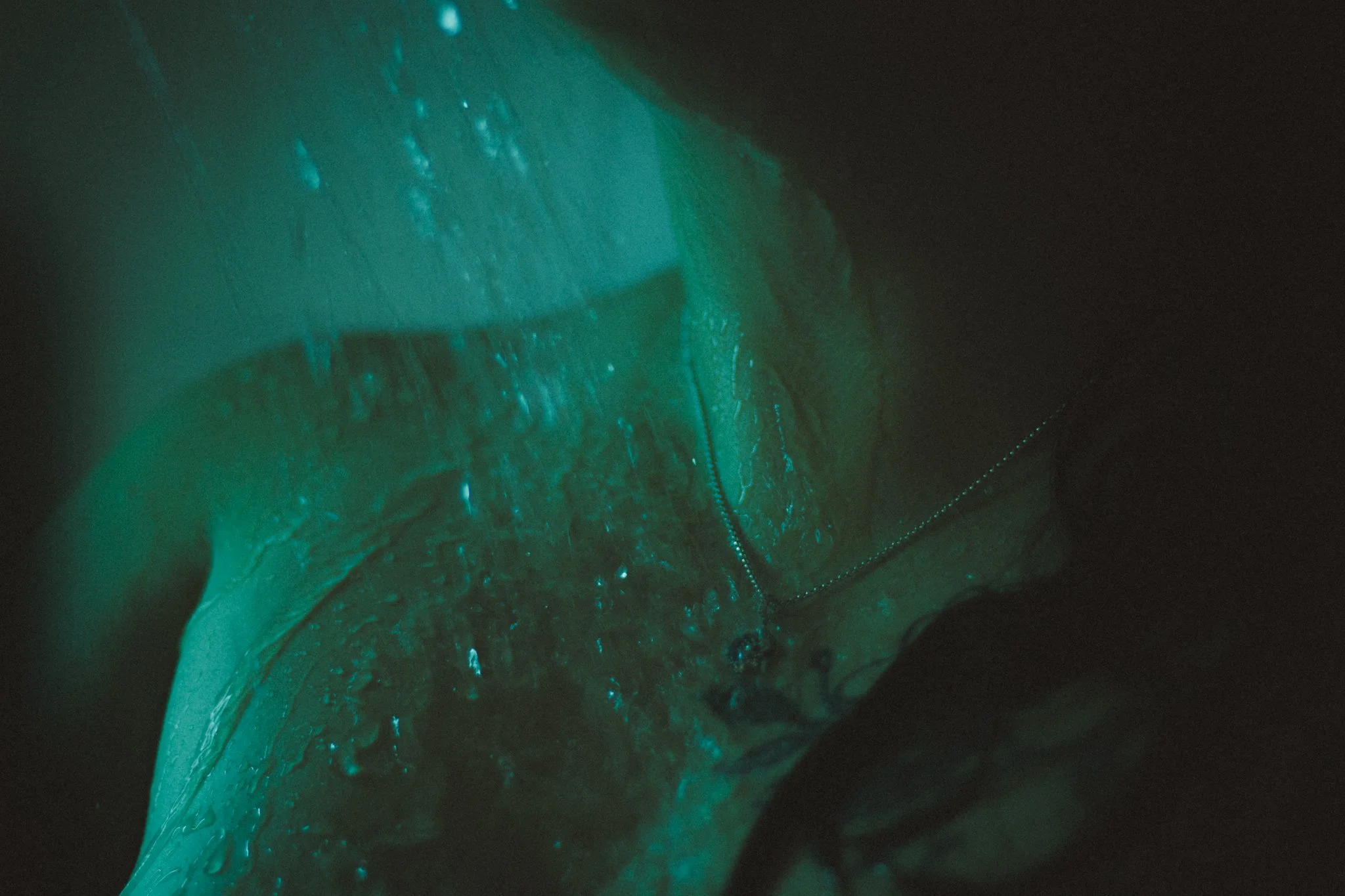 Close-up of a person wearing a jacket with water droplets, illuminated with greenish-blue light, against a dark background.