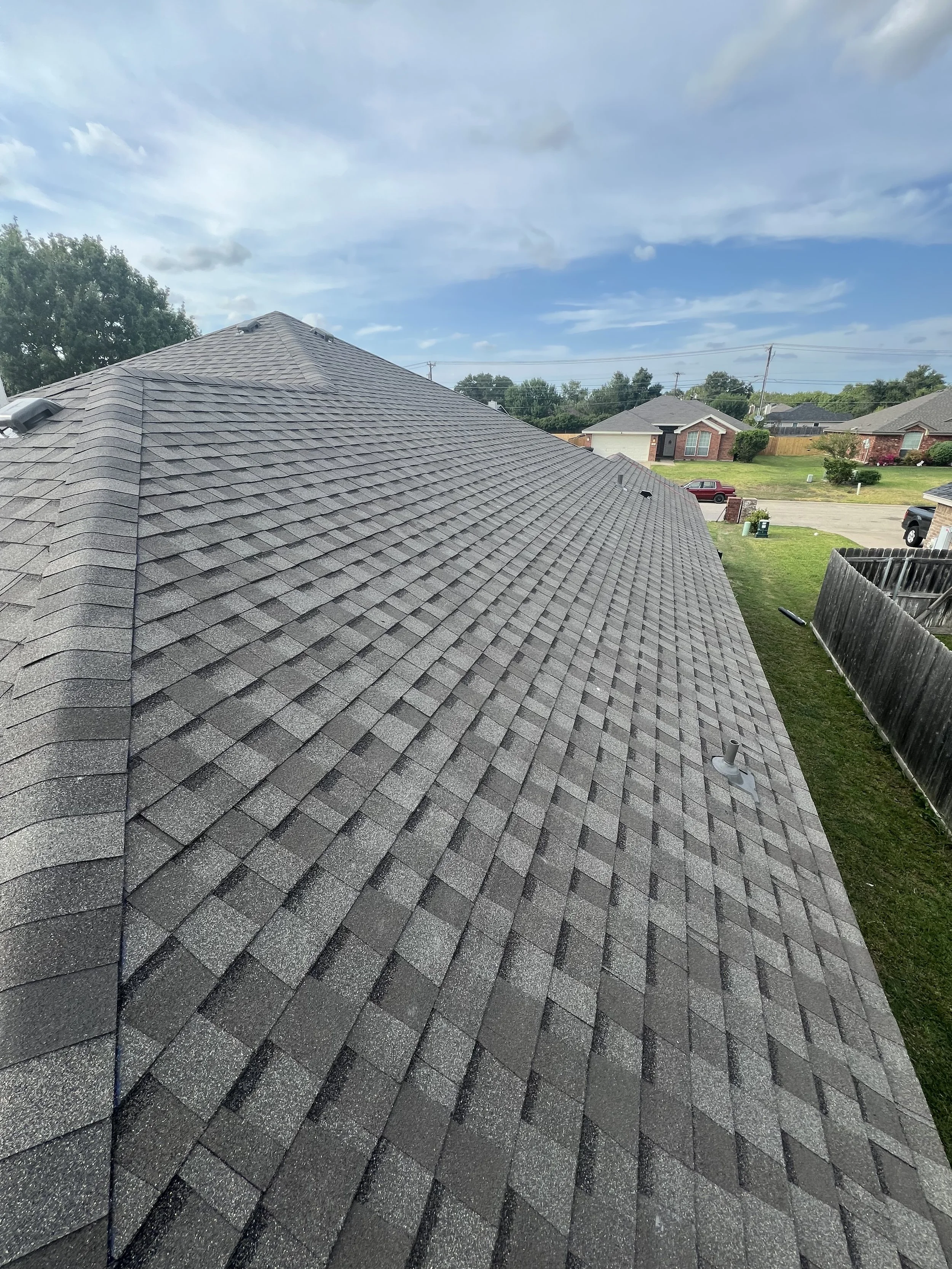 Gray asphalt shingle roof on a suburban home, under a partly cloudy sky.