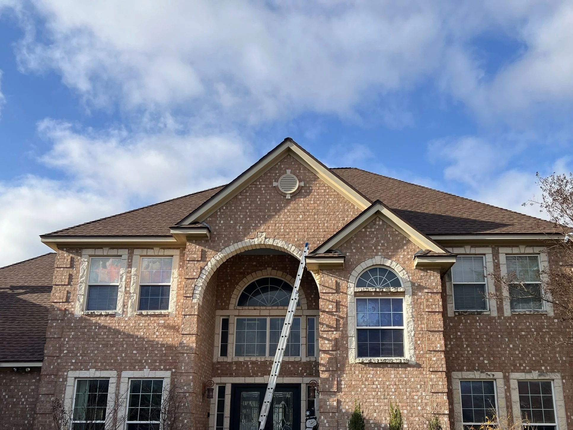 Two-story brick house facade with arched windows and a ladder leaning against it under a blue sky.