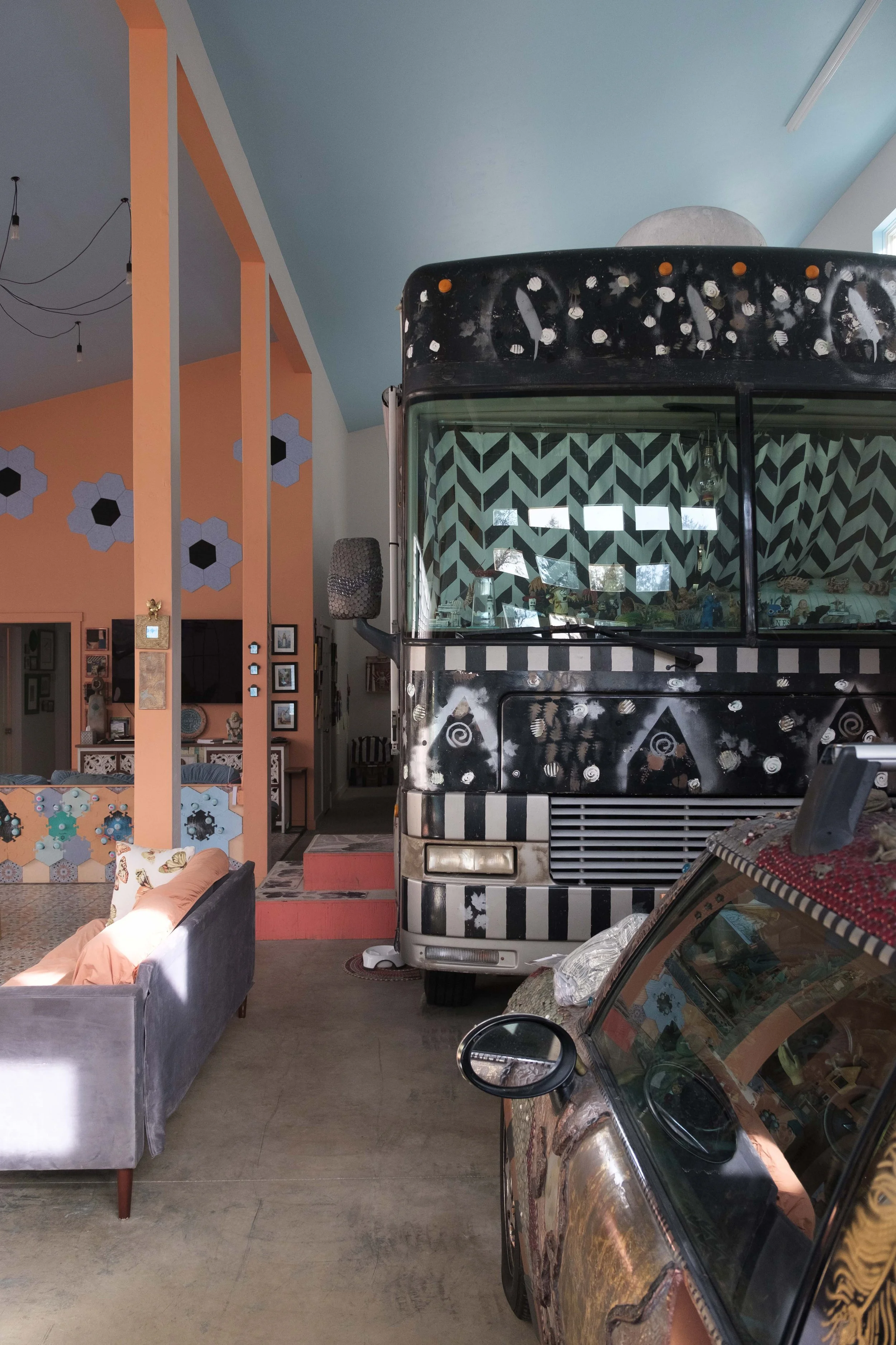 Interior of a house with a vintage bus and a car, colorful geometric wall decor, and eclectic furniture.