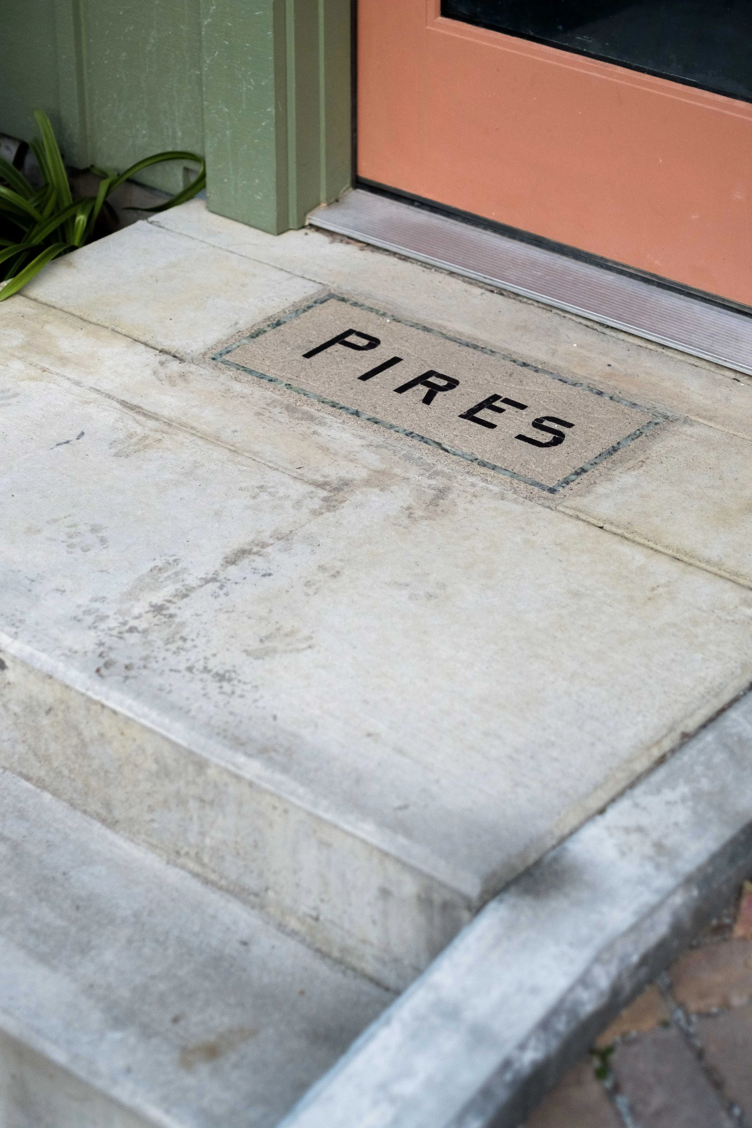 Concrete step with a metal plaque engraved with the word 'Pires' near a door with a peach-colored frame.