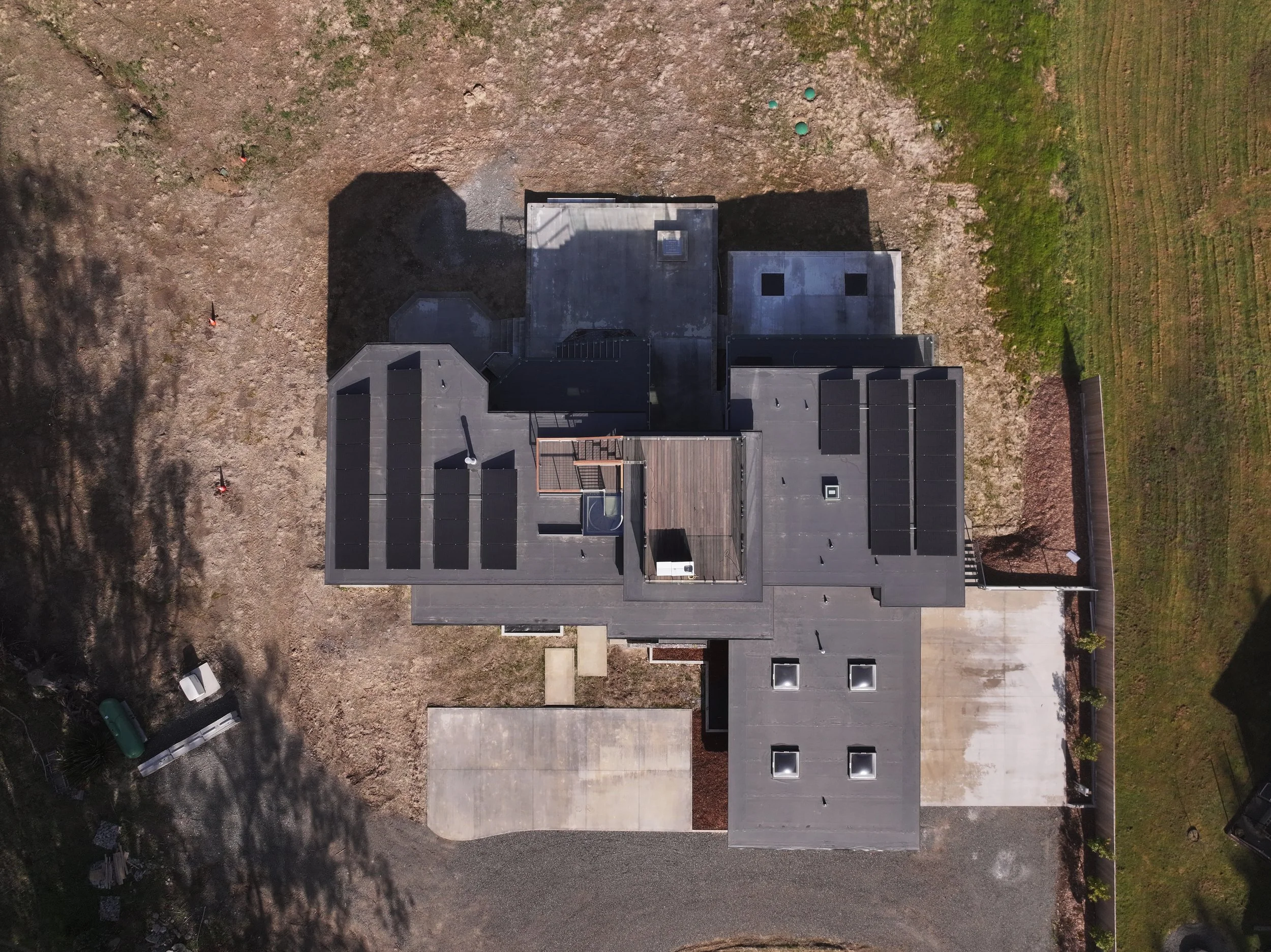 Aerial view of a house with solar panels on its roof, surrounded by a yard with a concrete driveway and lawn.