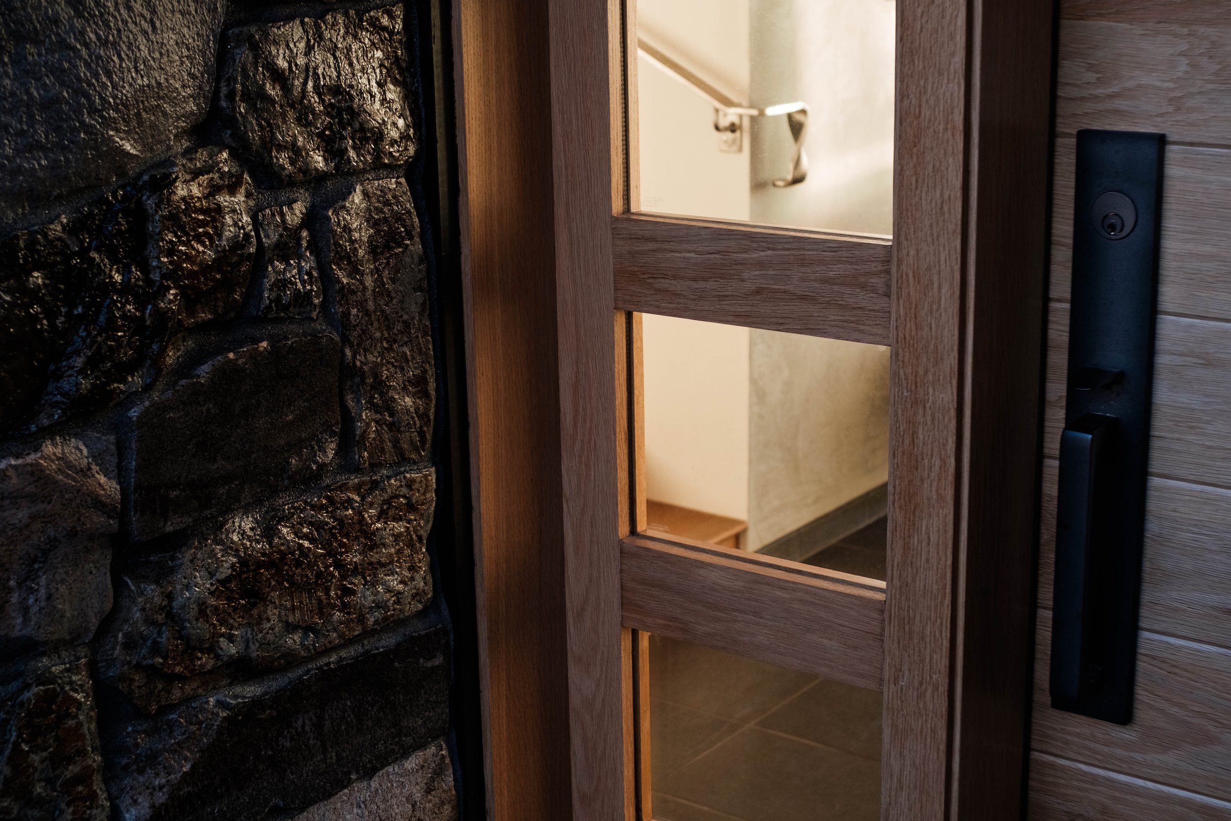 Close-up view of a wooden door with horizontal slats, black door handle, and a stone wall adjacent to it.