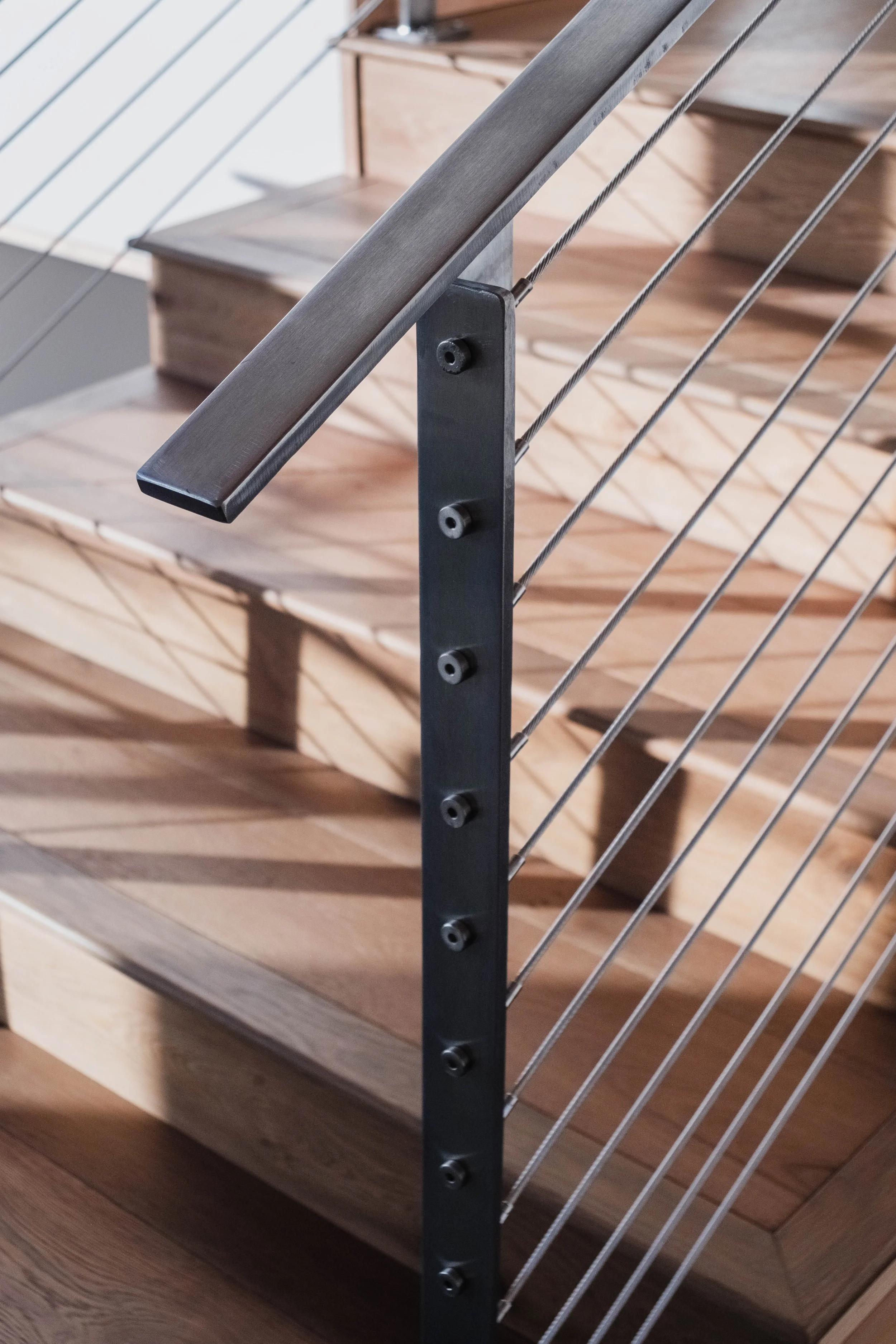 Close-up view of a modern staircase with wooden steps, a metal handrail, and horizontal metal cable railing.