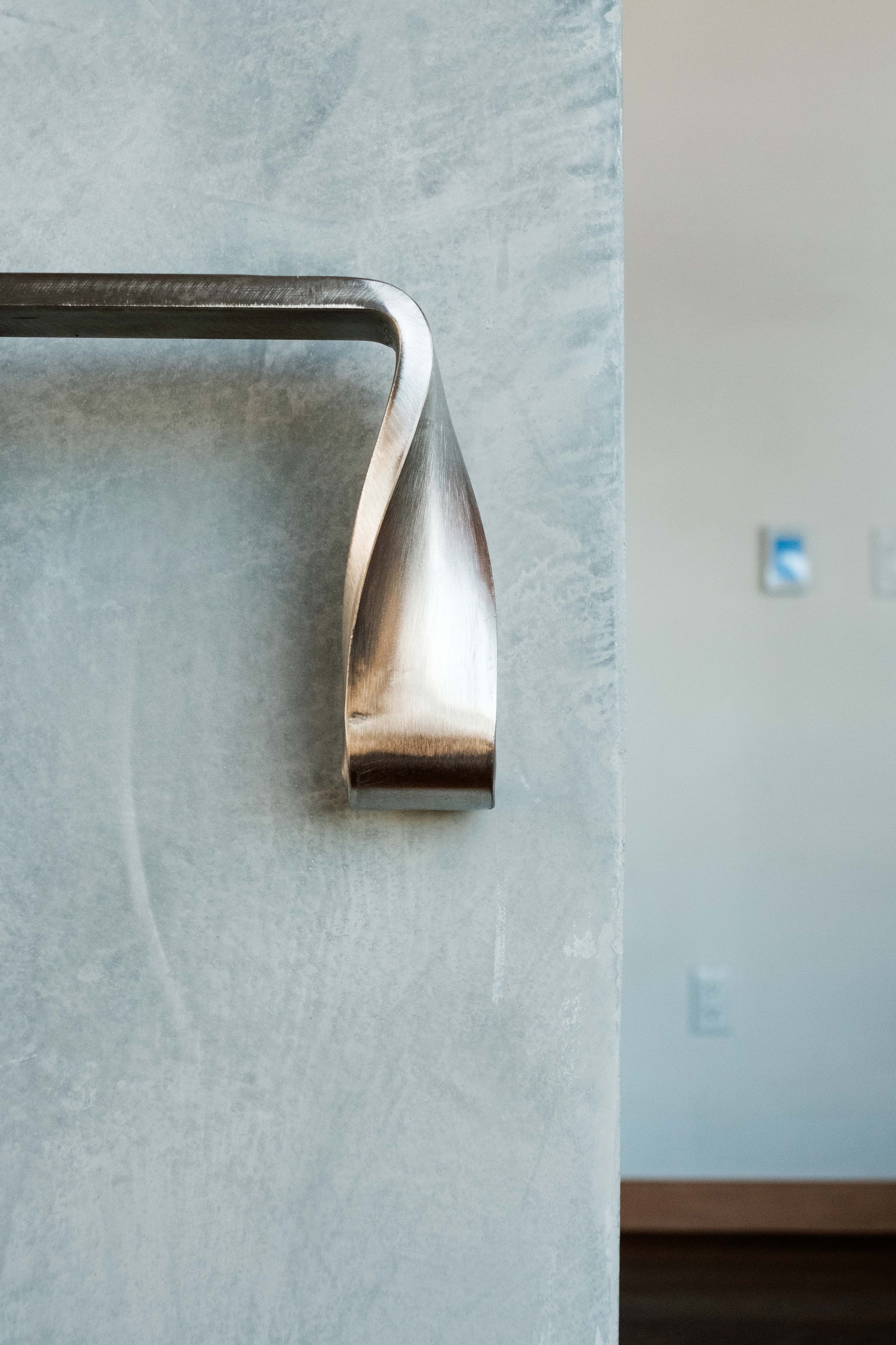 Close-up of a metallic handrail attached to a textured wall, with a neutral-colored wall and electrical outlets in the background.