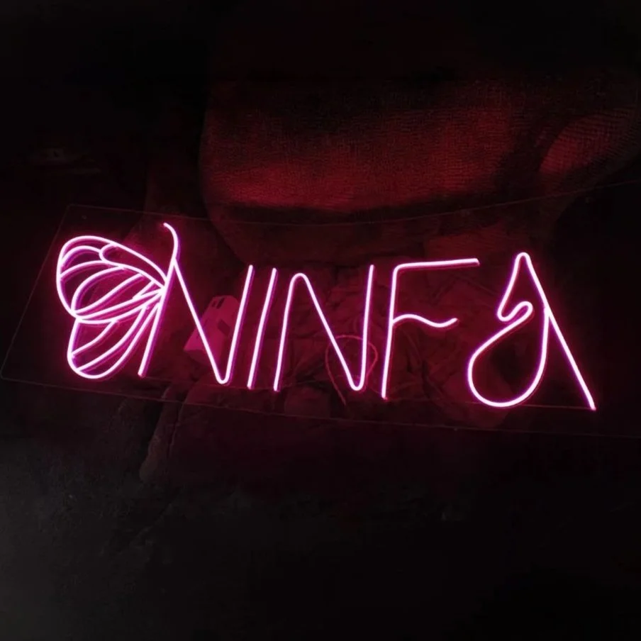 Letrero de neón rosa que dice 'NINA' con una mariposa de neón a la izquierda.
