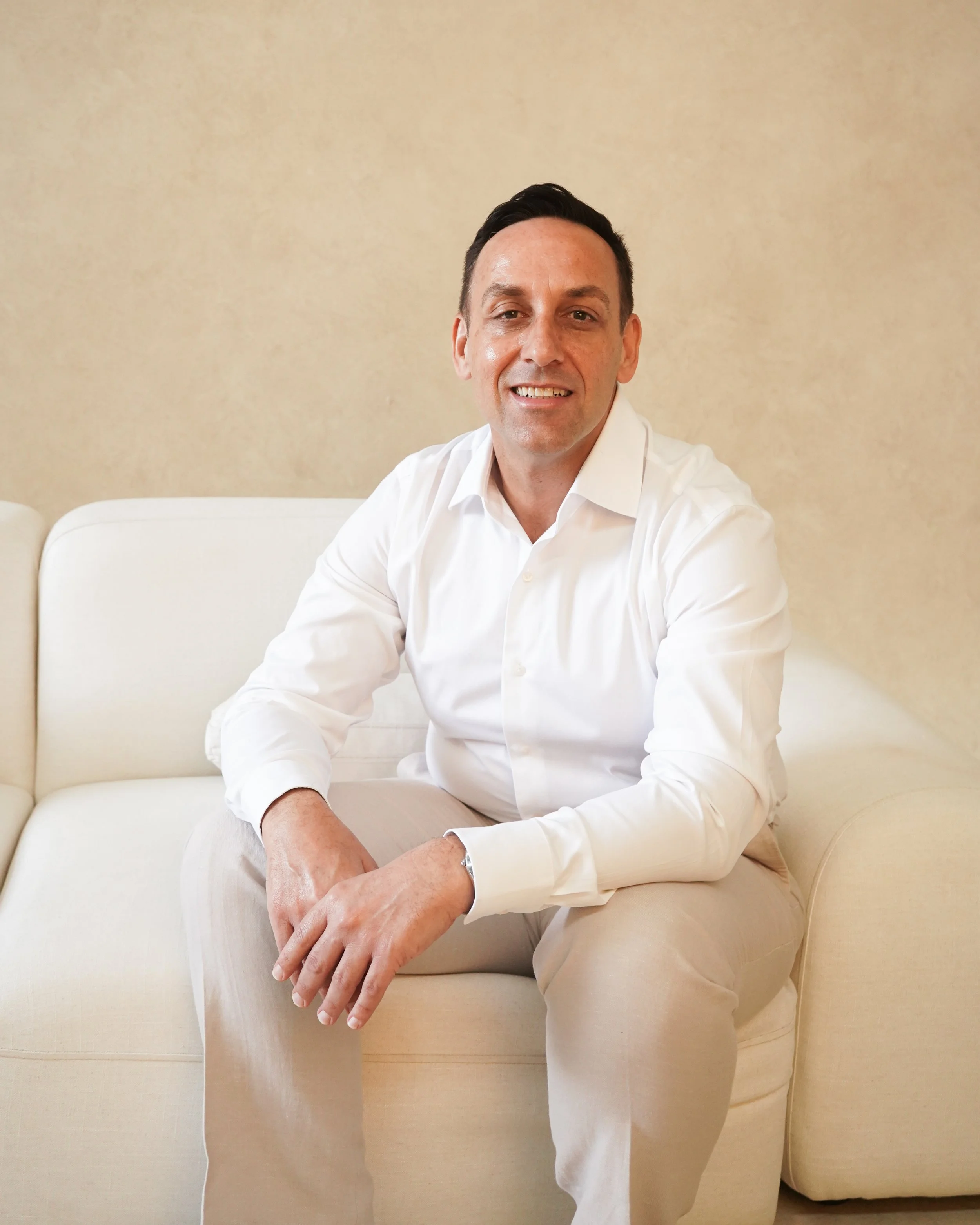 Man in a suit sitting on a stool, smiling