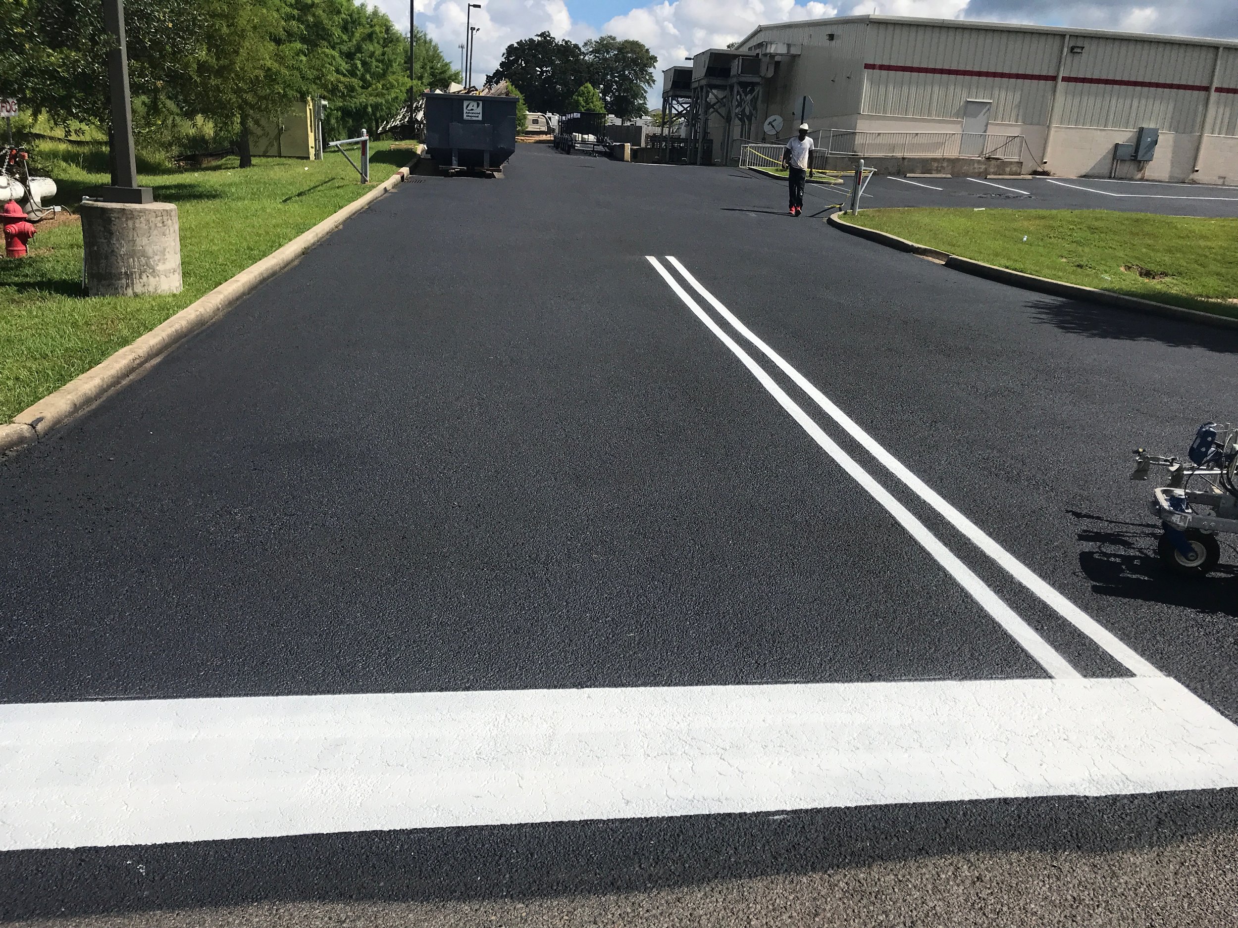 A construction worker paves a road, applying white lines to mark lanes on the freshly laid asphalt surface.