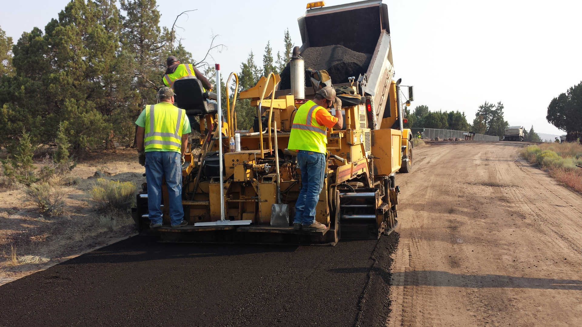 A team of men engaged in road construction, equipped with tools and wearing reflective vests for safety.