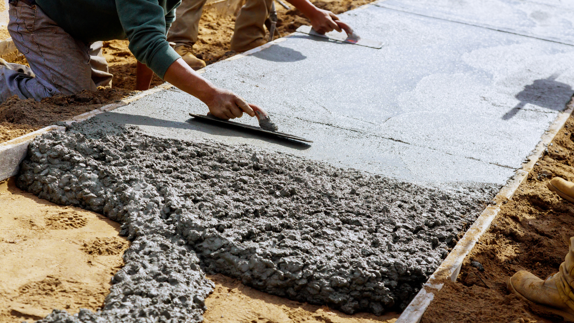 A man applying concrete to a sidewalk, focused on smoothing the surface with a trowel.