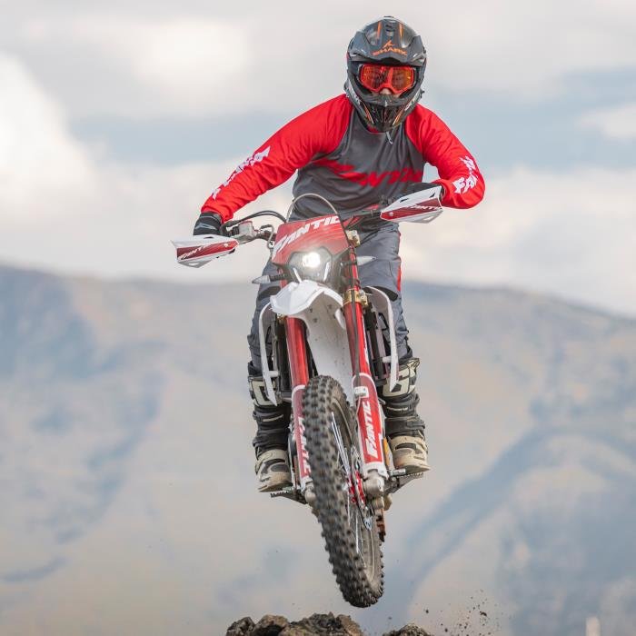 Motorcyclist performing jump on dirt bike in mountainous terrain.