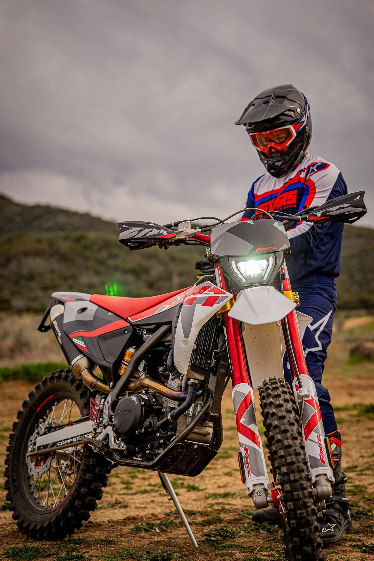 Person in riding gear and helmet gets ready to ride a red and white motorcycle.