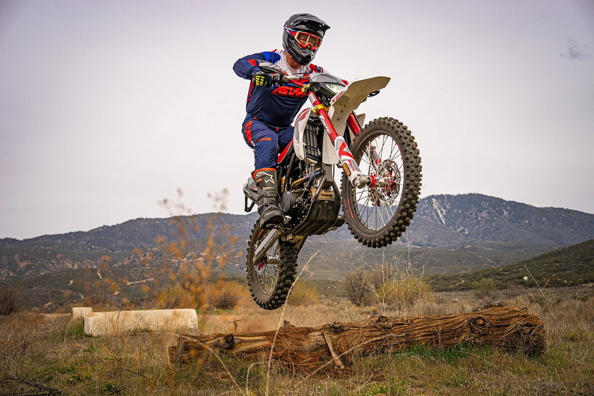 Person jumping a motorcycle over a fallen log.