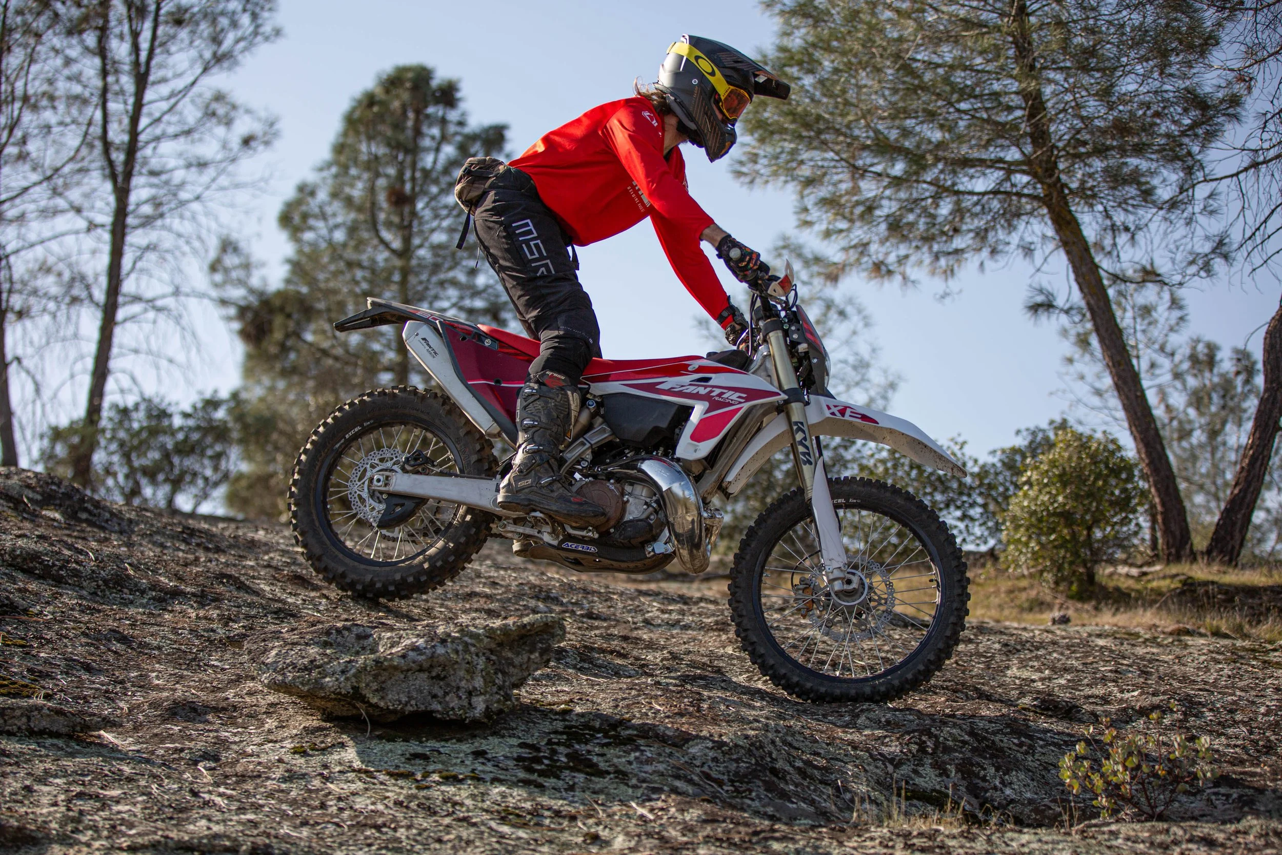 Dirt bike rider in red jersey rides motorcycle on a rock slab.
