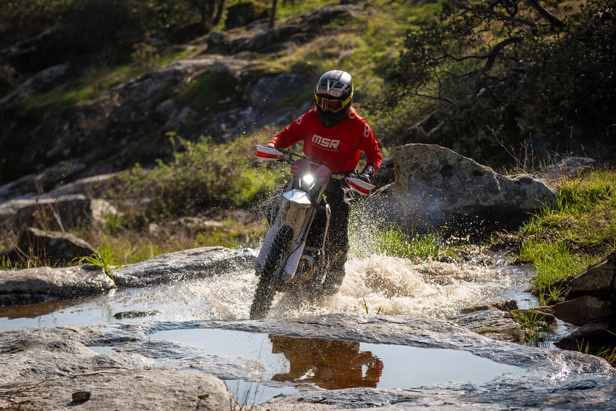Dirt bike splashes through a stream crossing.