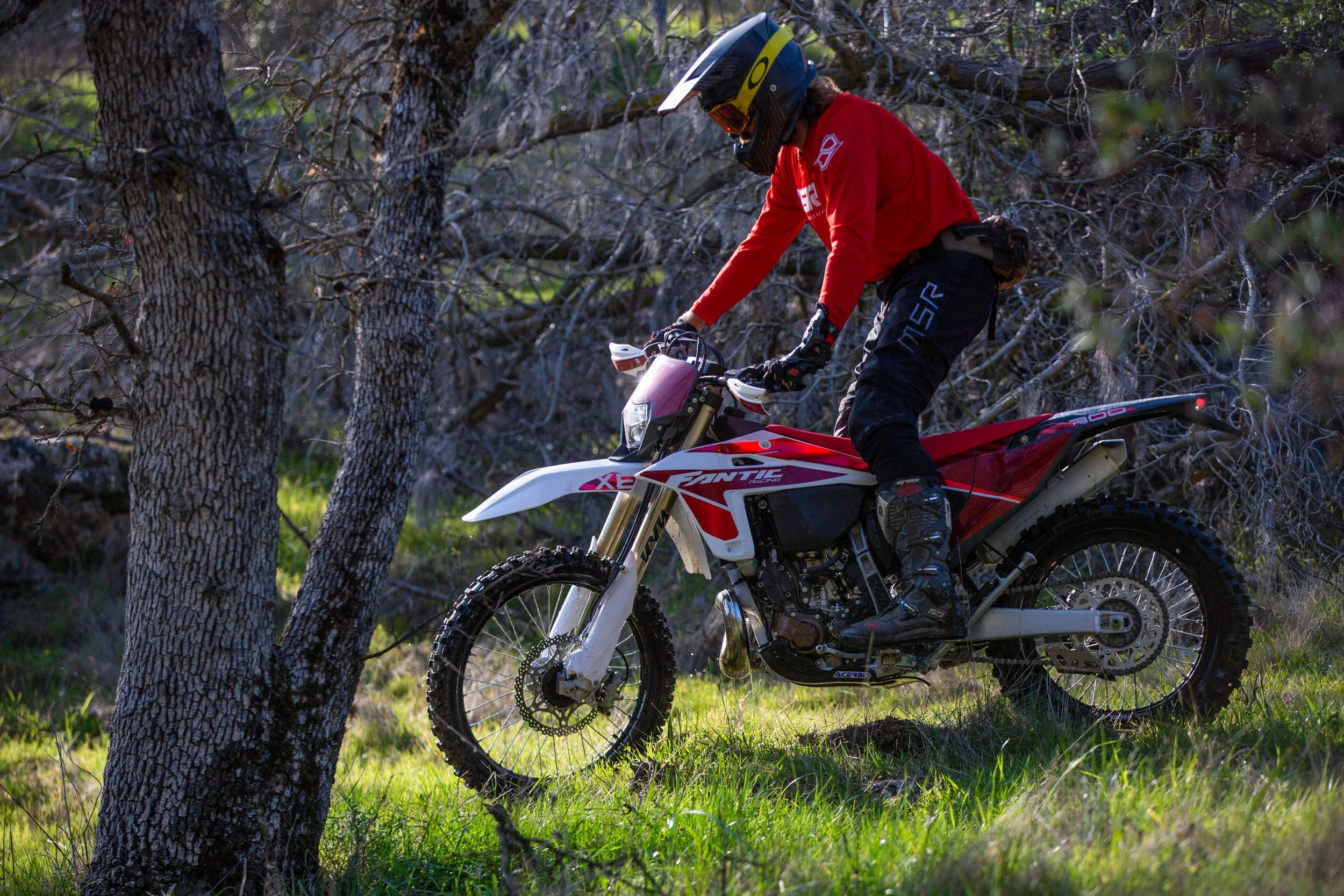 Person riding a dirt bike through the woods and green grass.