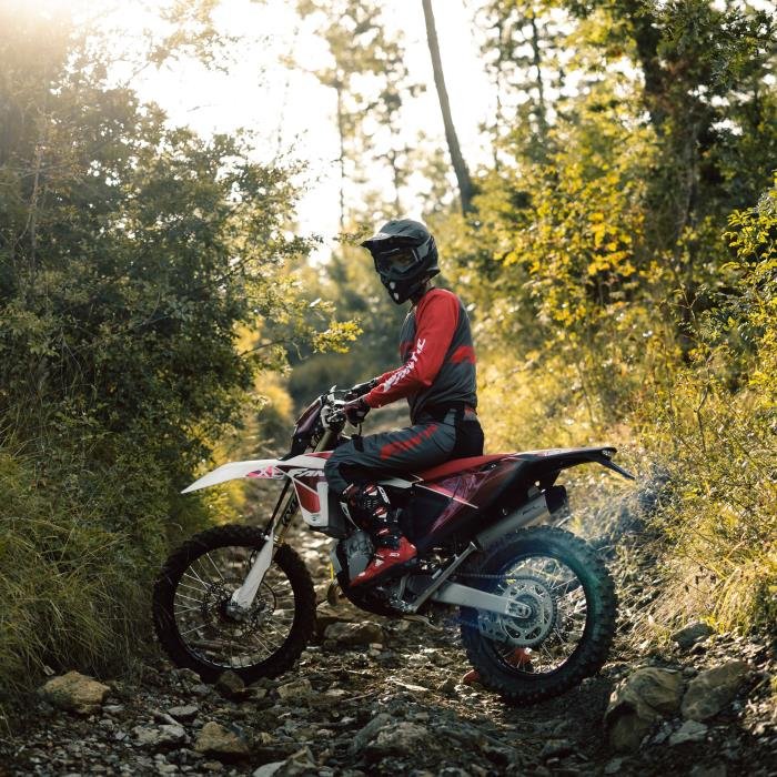 Person in motorcycle gear on dirt bike in forested area