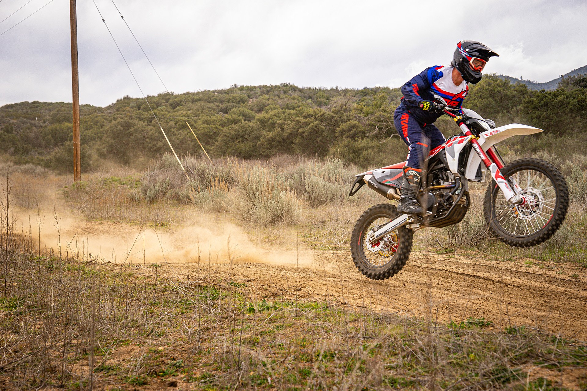 Dirt bike rider racing at high speed down a dusty trail.